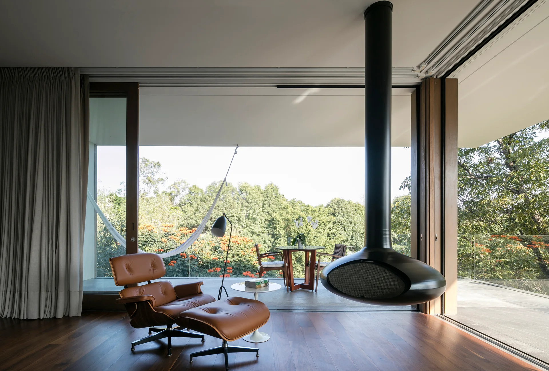A brown leather lounge chair and black suspended fireplace sit near open sliding glass doors leading to a green terrace.