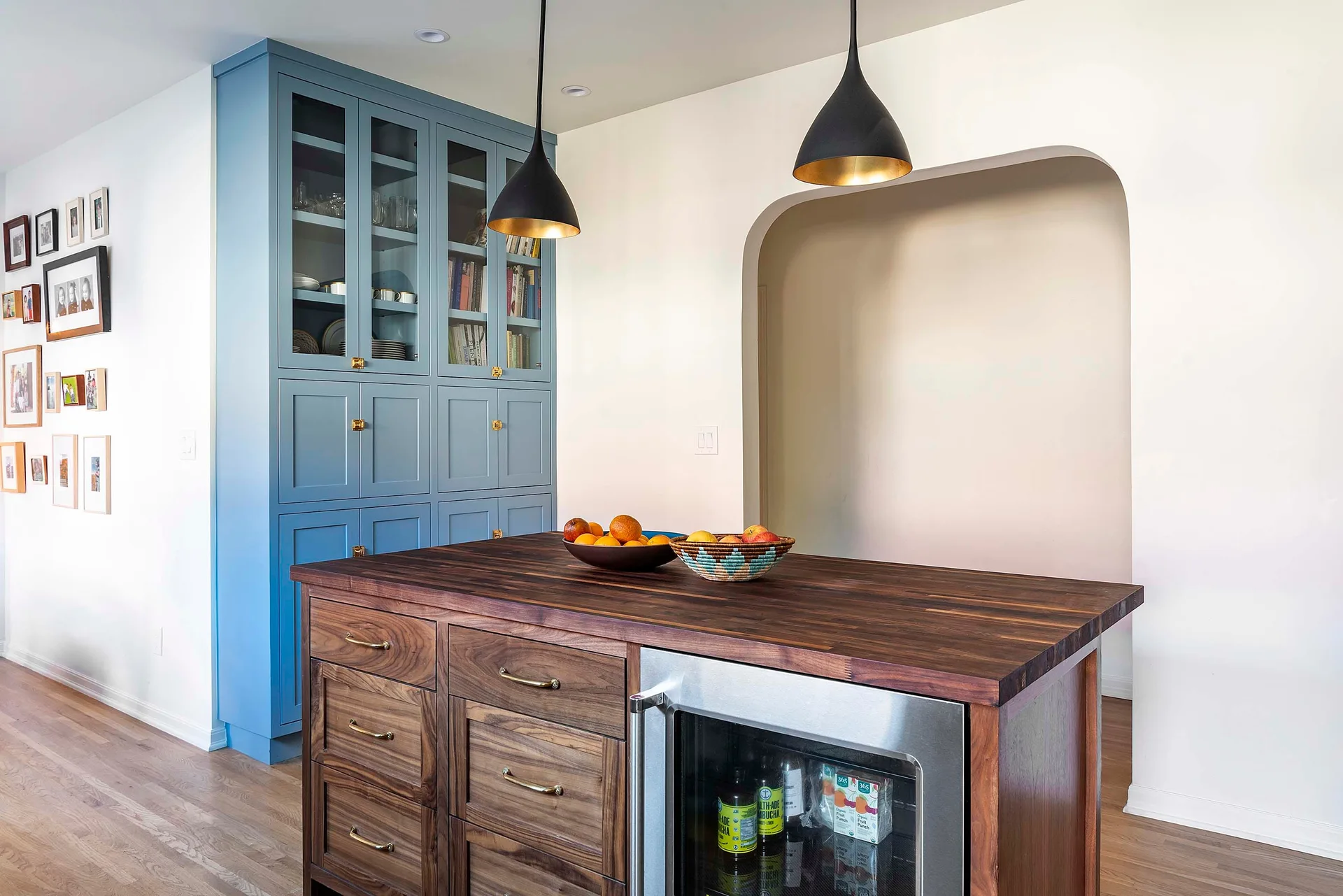 A kitchen featuring a walnut butcher block island with a beverage fridge, blue built-in cabinets, and black dome pendant lights.