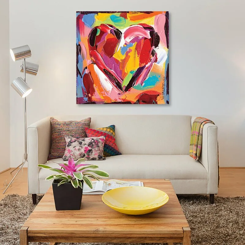 A beige sofa sits below a colorful heart painting, accompanied by a wooden coffee table and a metallic floor lamp.