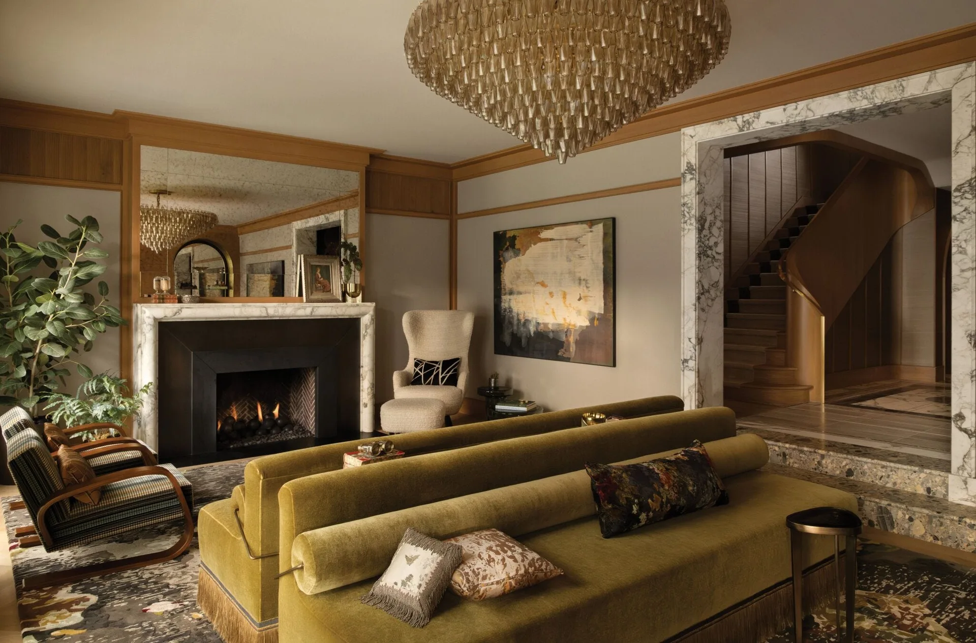 An olive green velvet sofa sits in a living room featuring a marble fireplace, a tiered crystal chandelier, and a marble-framed archway leading to stairs.
