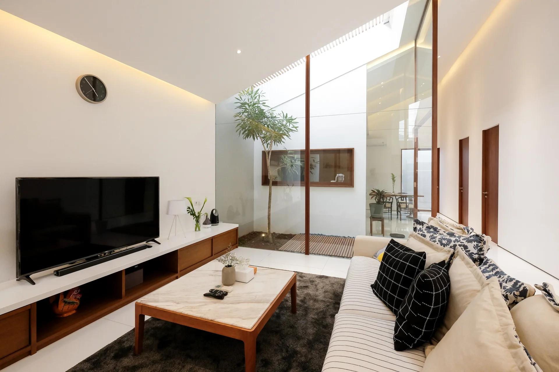 A minimalist living room with a striped sofa, a stone-top coffee table, and an internal glass-walled courtyard.
