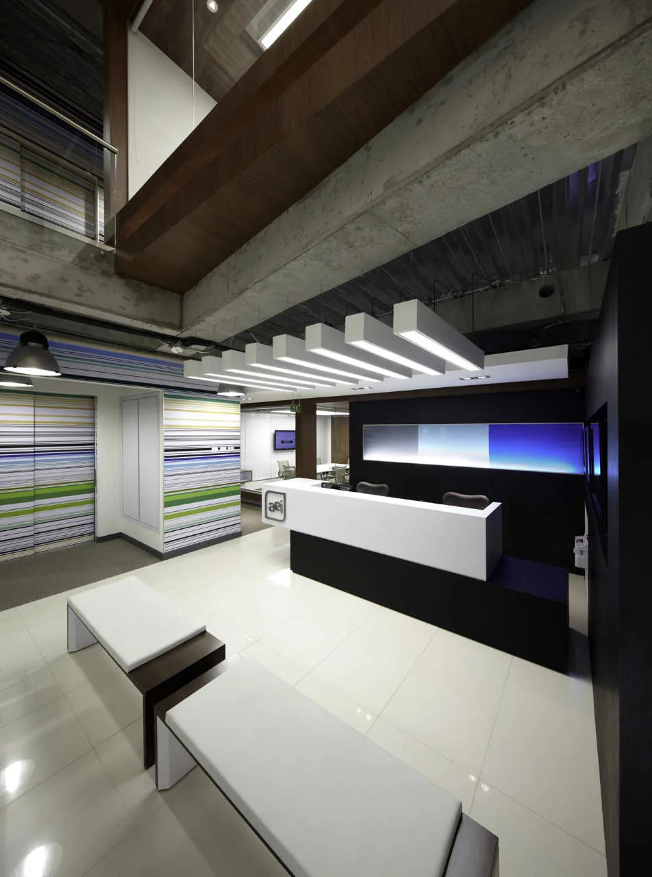 A modern office reception area features a black and white reception desk, parallel linear ceiling lights, and two white benches on glossy tile floors.