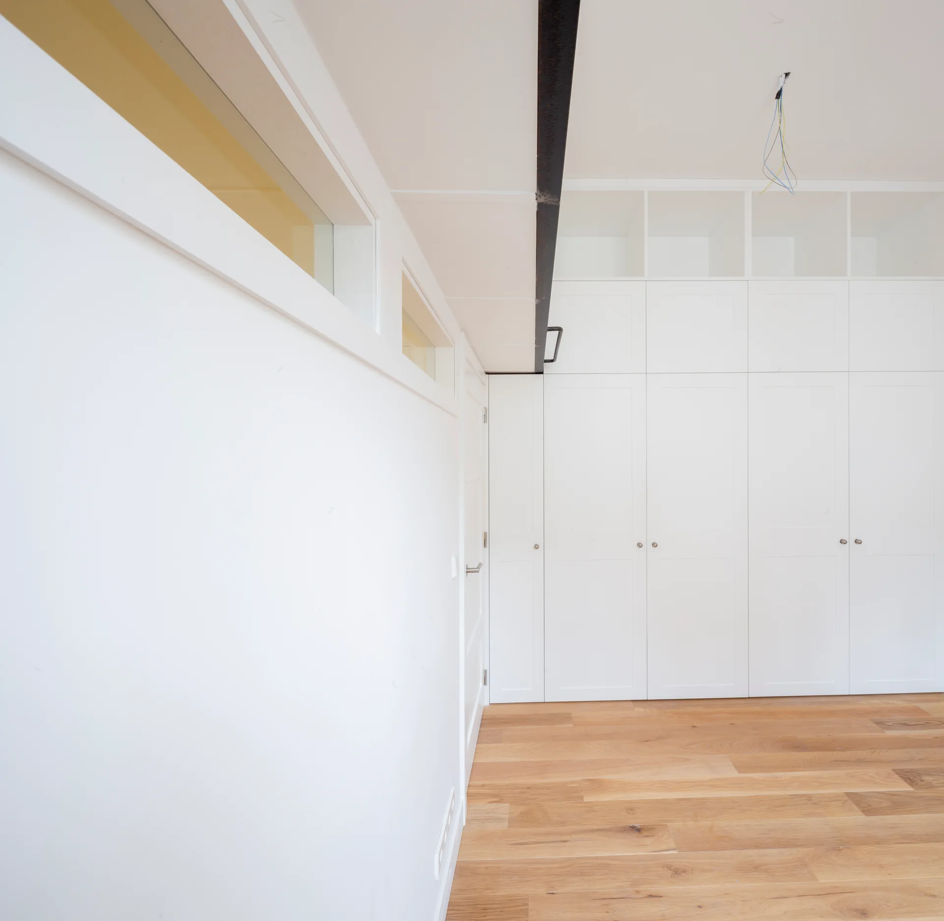 White floor-to-ceiling built-in storage cabinets stand next to a light wood floor and an interior wall with rectangular transom windows.