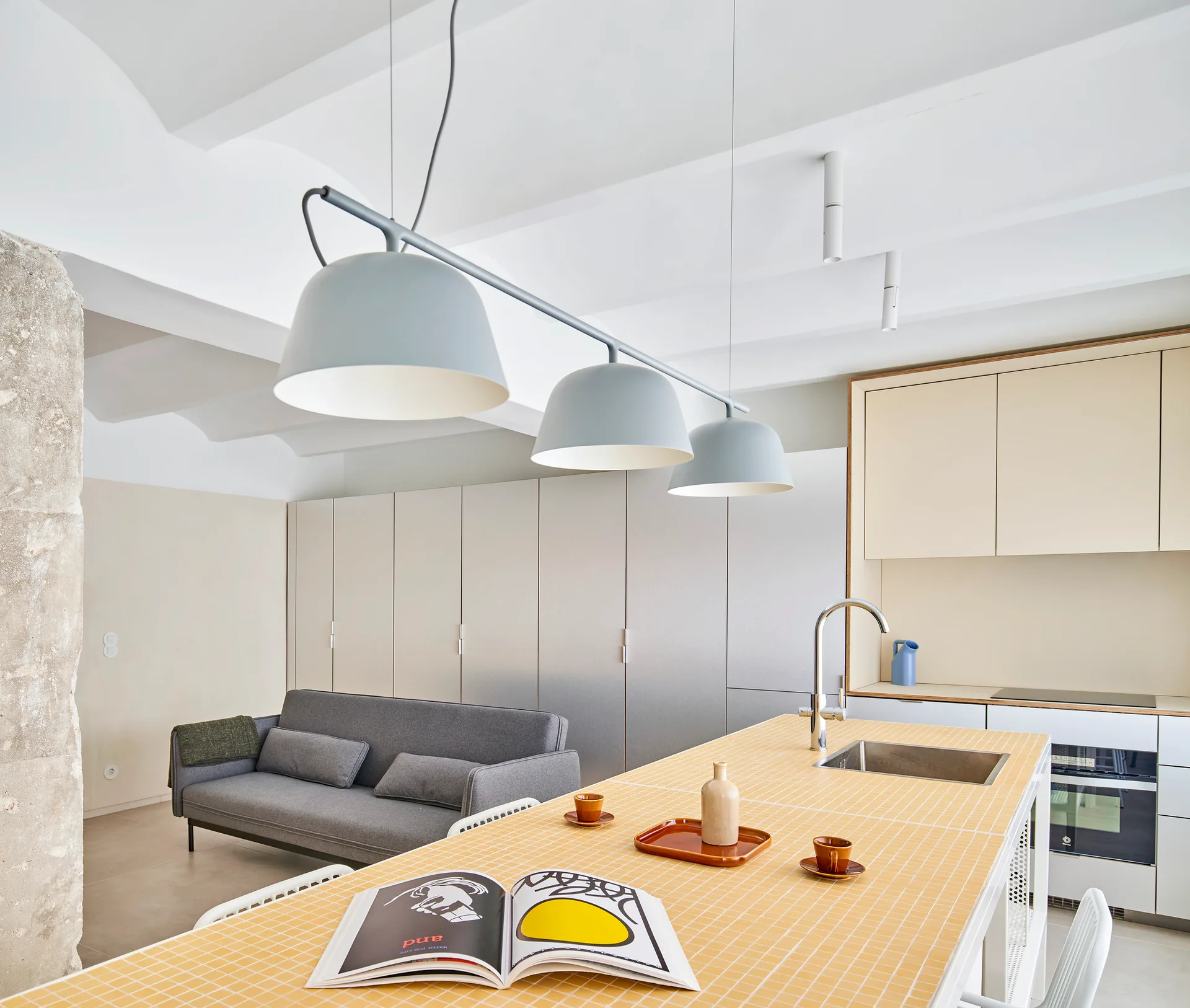 A modern open concept kitchen features a yellow tiled island with a sink and a grey sofa in the adjacent living space.