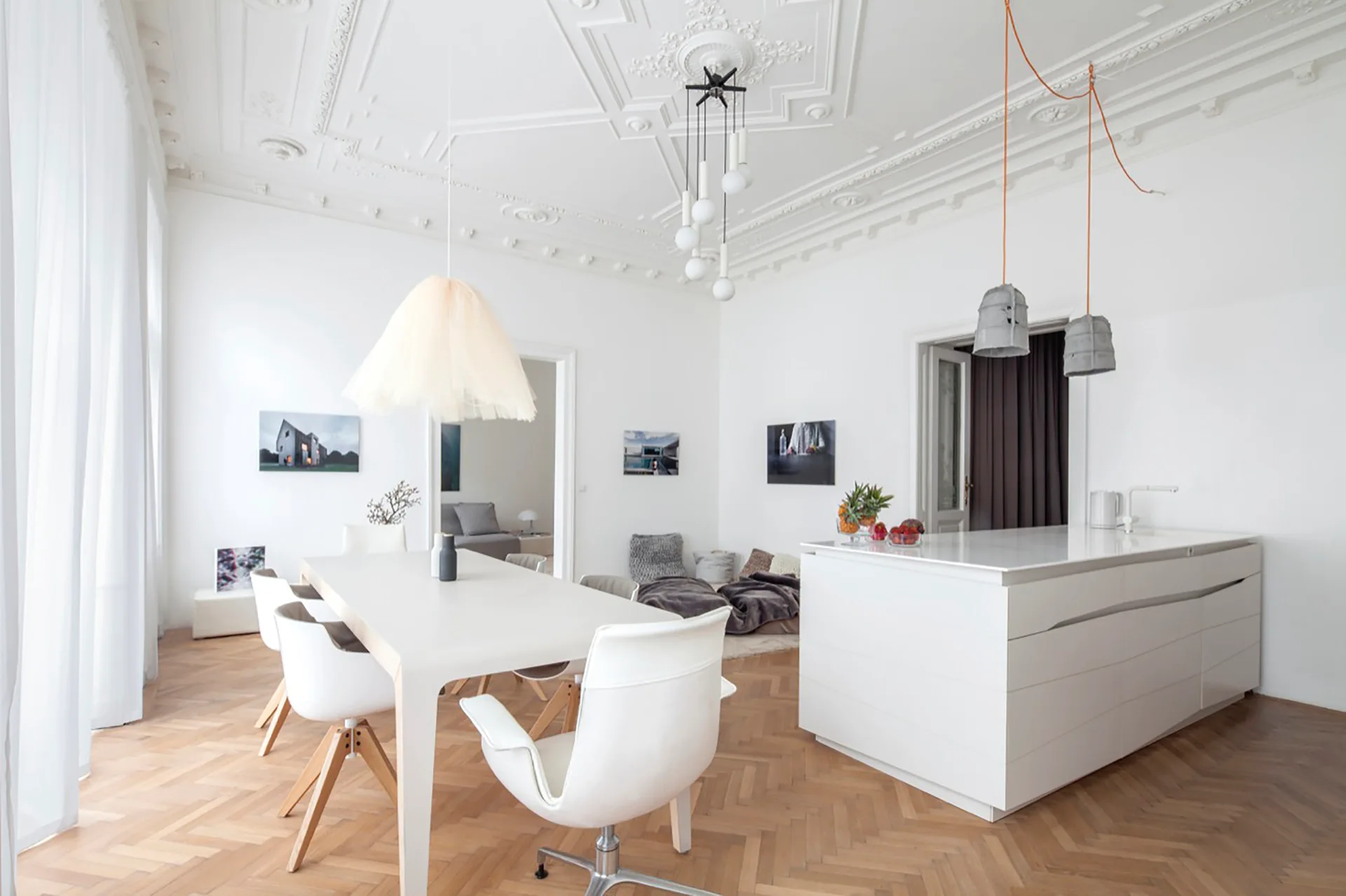 A white open-concept dining room and kitchen featuring modern furniture, a herringbone wood floor, and decorative ceiling plasterwork.