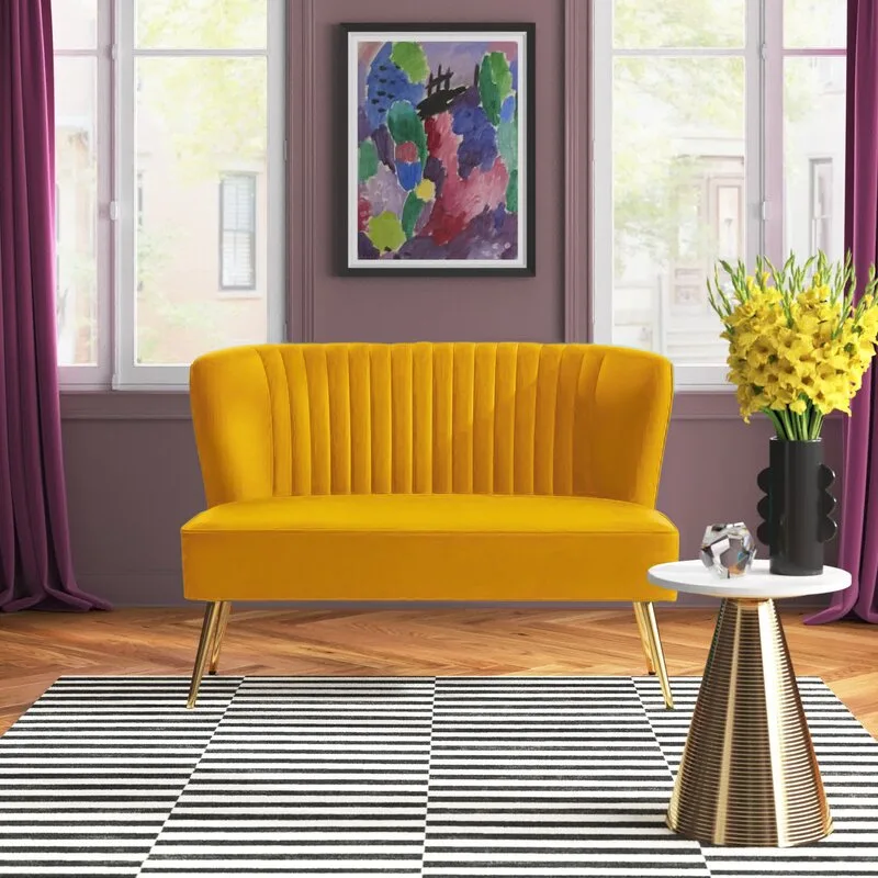 A yellow velvet settee sits on a black and white striped rug in front of a deep purple wall with matching drapes.