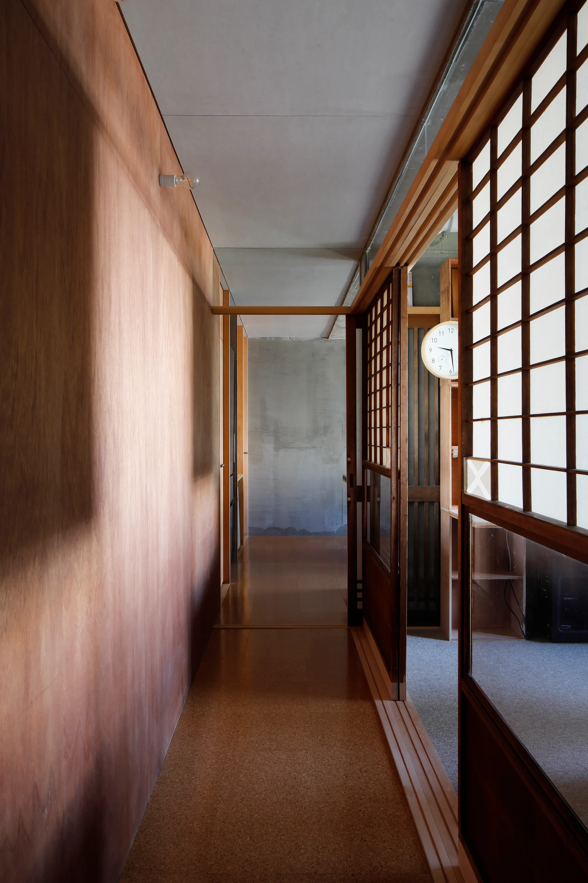 A narrow interior hallway features warm wood-paneled walls, sliding wooden grid shoji doors, and a gray concrete wall at the end.