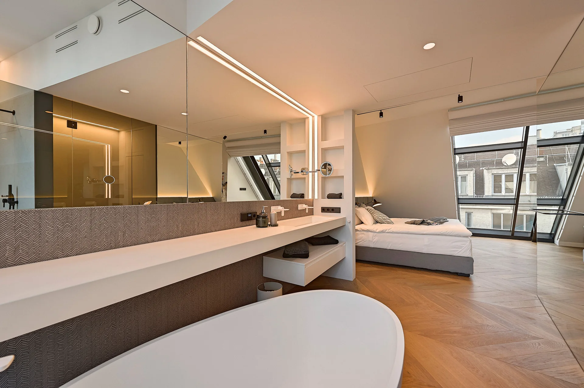 An open-concept bedroom suite features a white freestanding bathtub and a vanity separated from the bed by a partial wall divider.