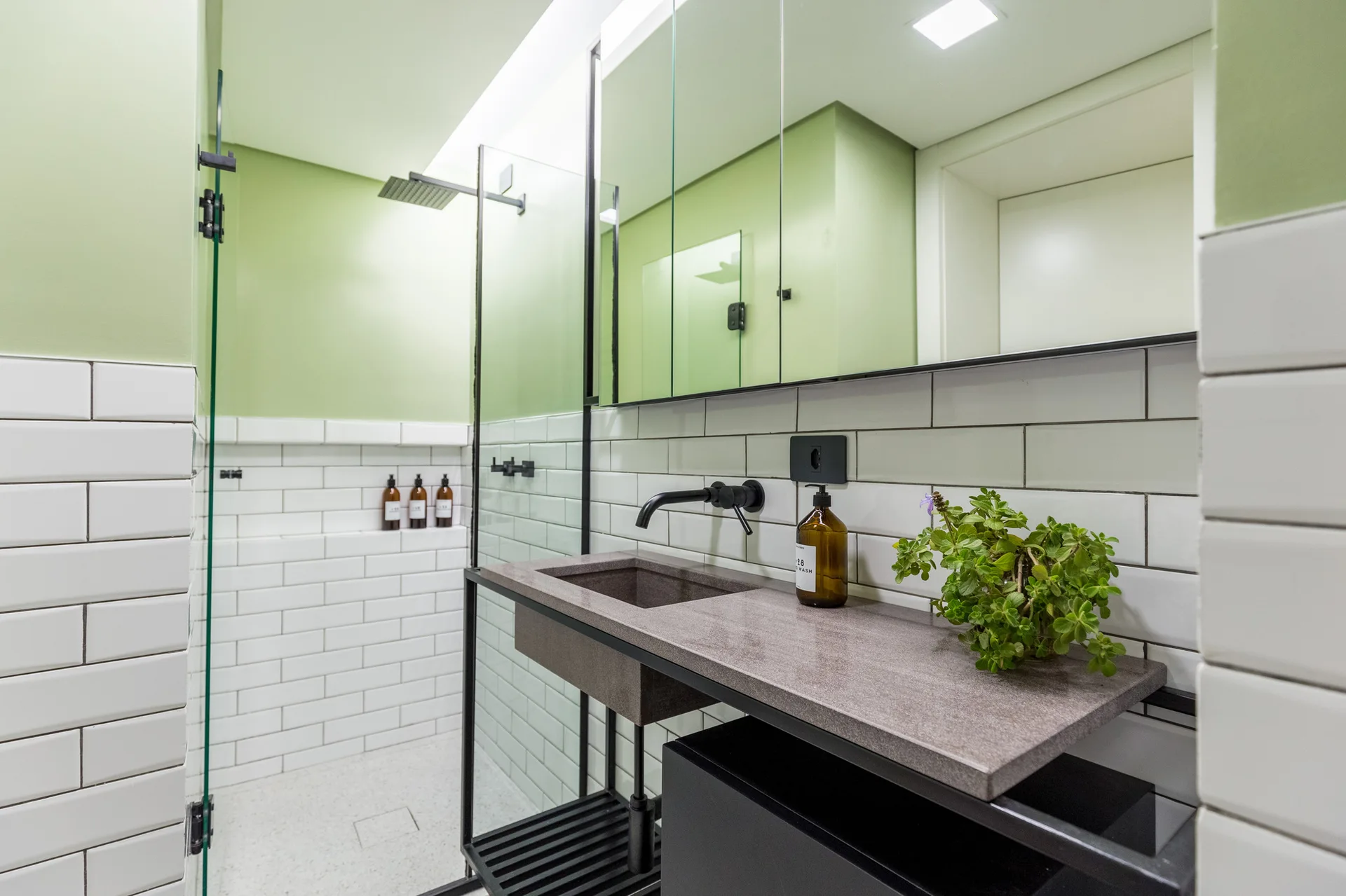 A modern bathroom features a grey stone vanity, matte black fixtures, white subway tile walls, and a sage green upper accent wall.
