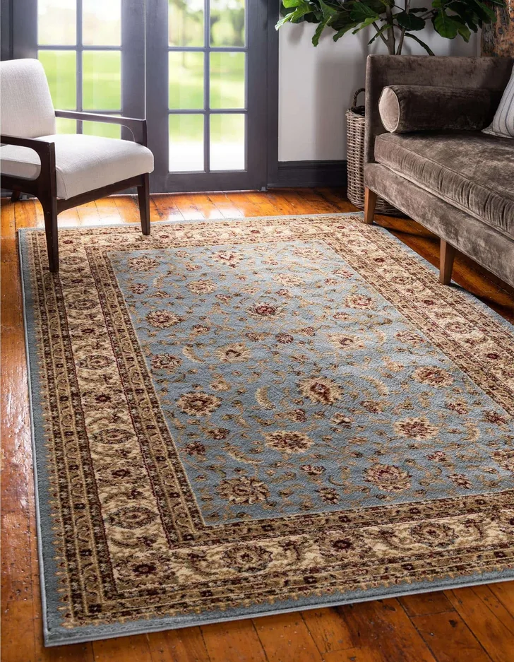 A traditional blue and red floral area rug lies on a glossy hardwood floor between a brown velvet sofa and a cream armchair.