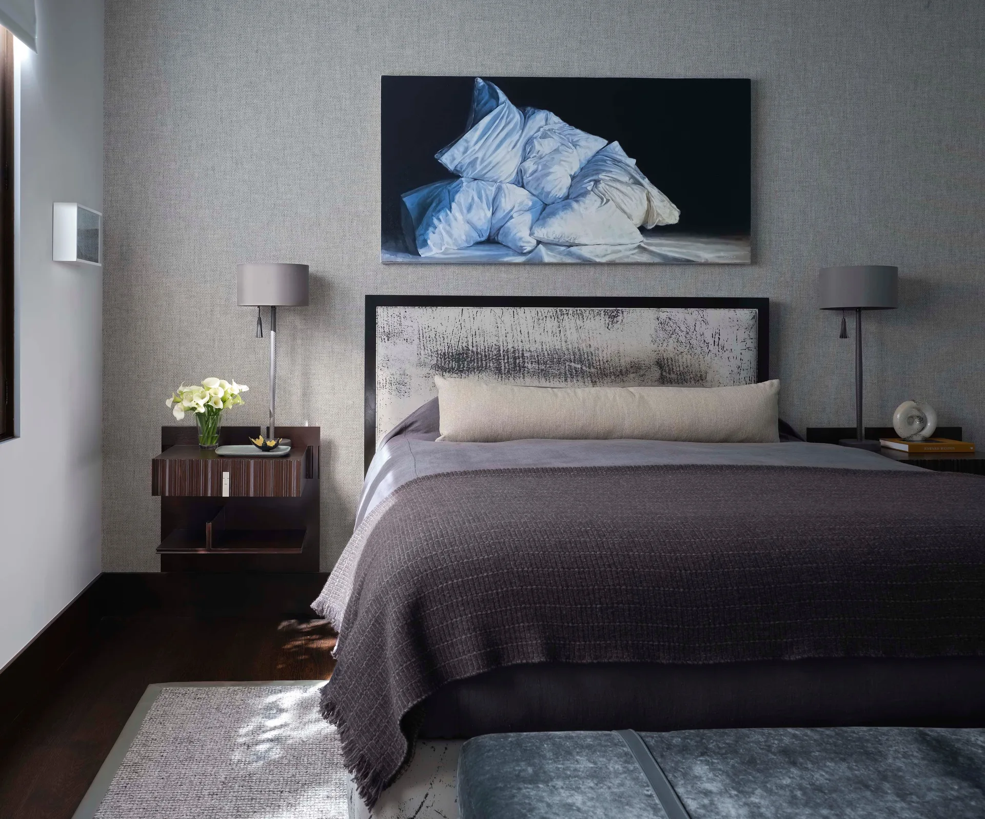 A contemporary bedroom with textured grey wallpaper, a patterned headboard, matching table lamps on floating nightstands, and charcoal bedding.