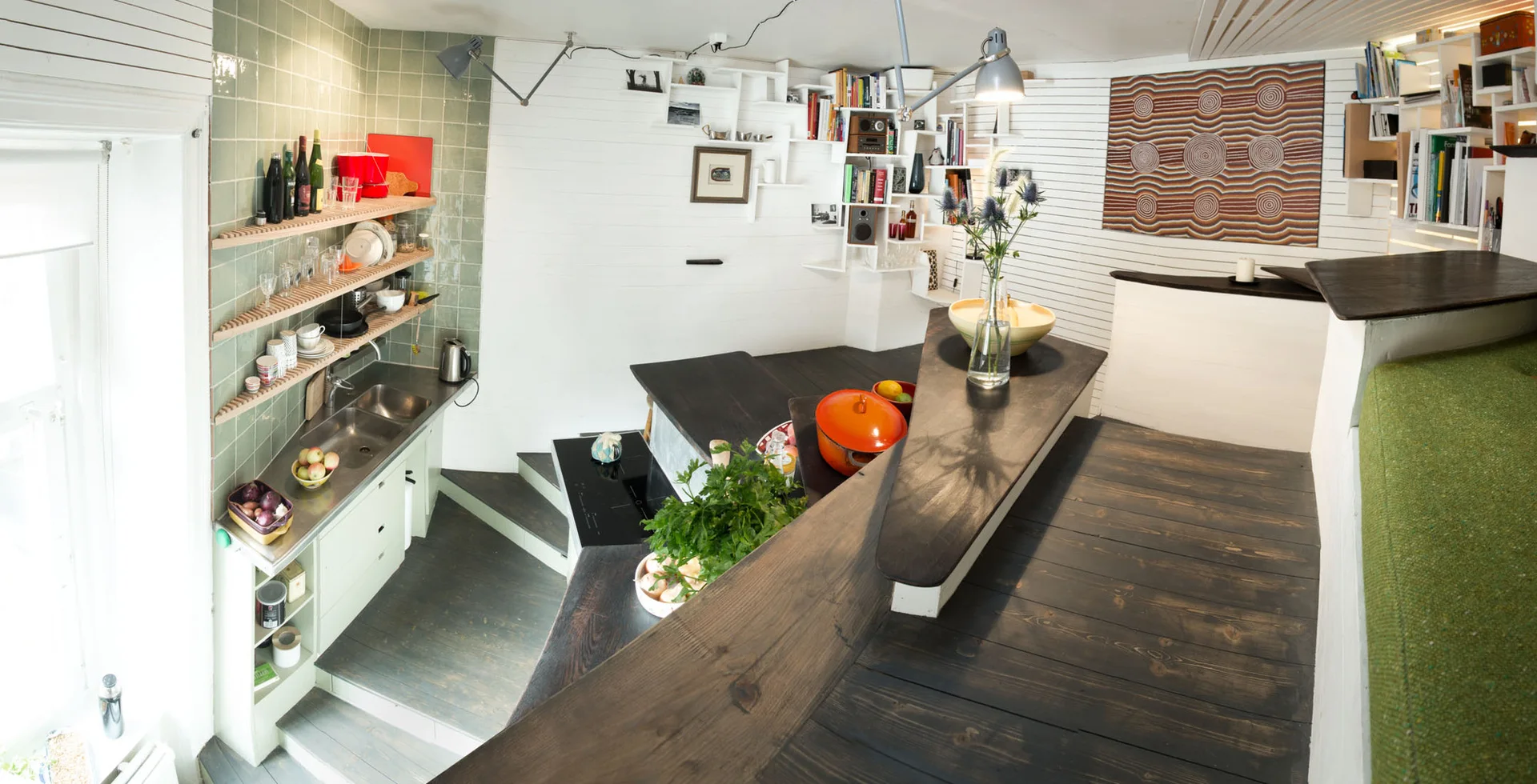 A sunken kitchen featuring a sage green tile backsplash, pale green cabinets, and dark wood countertops alongside a multi-level wooden floor.