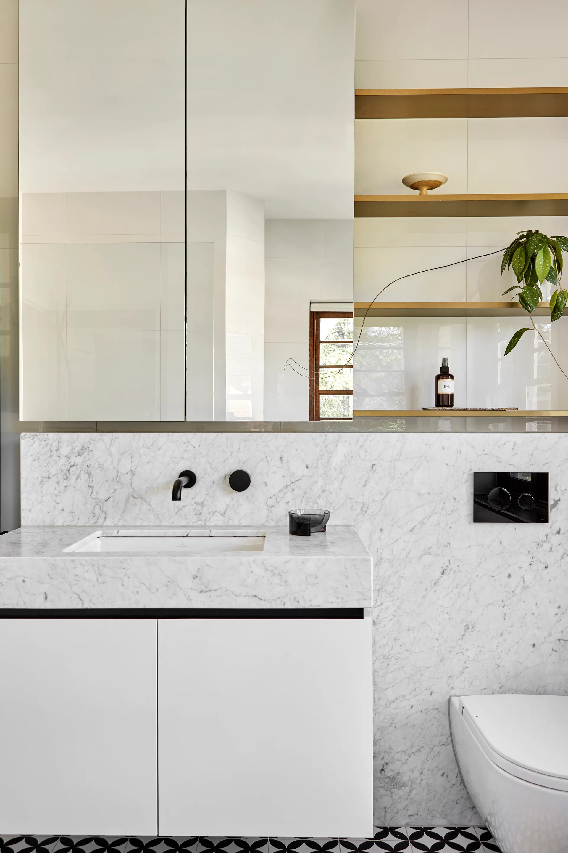 A white bathroom vanity features a marble countertop, wall-mounted black faucet, mirrored cabinet, and black-and-white geometric tile floor.