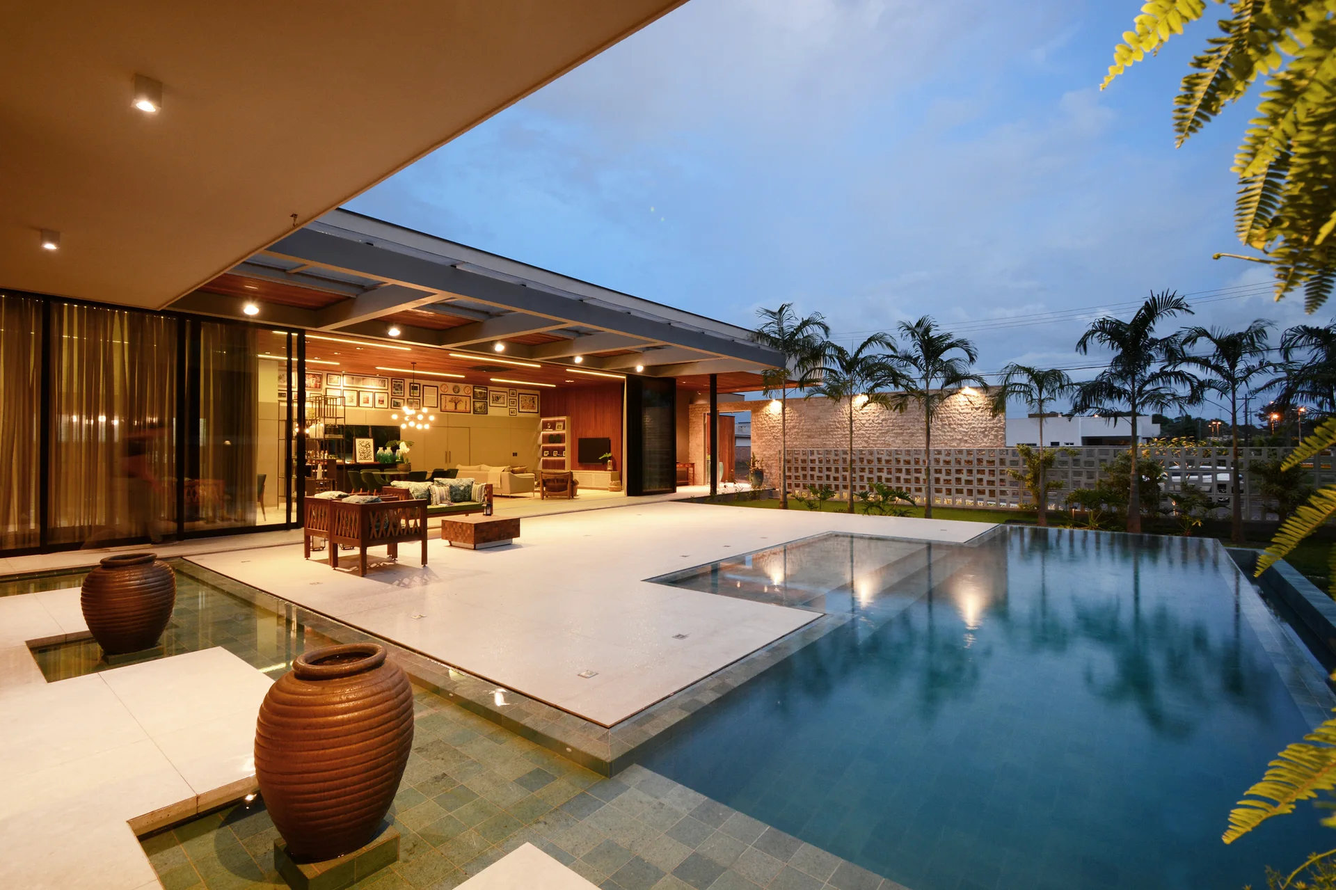 A contemporary patio with a rectangular swimming pool features large ceramic urns and a seamless transition to an indoor living area.