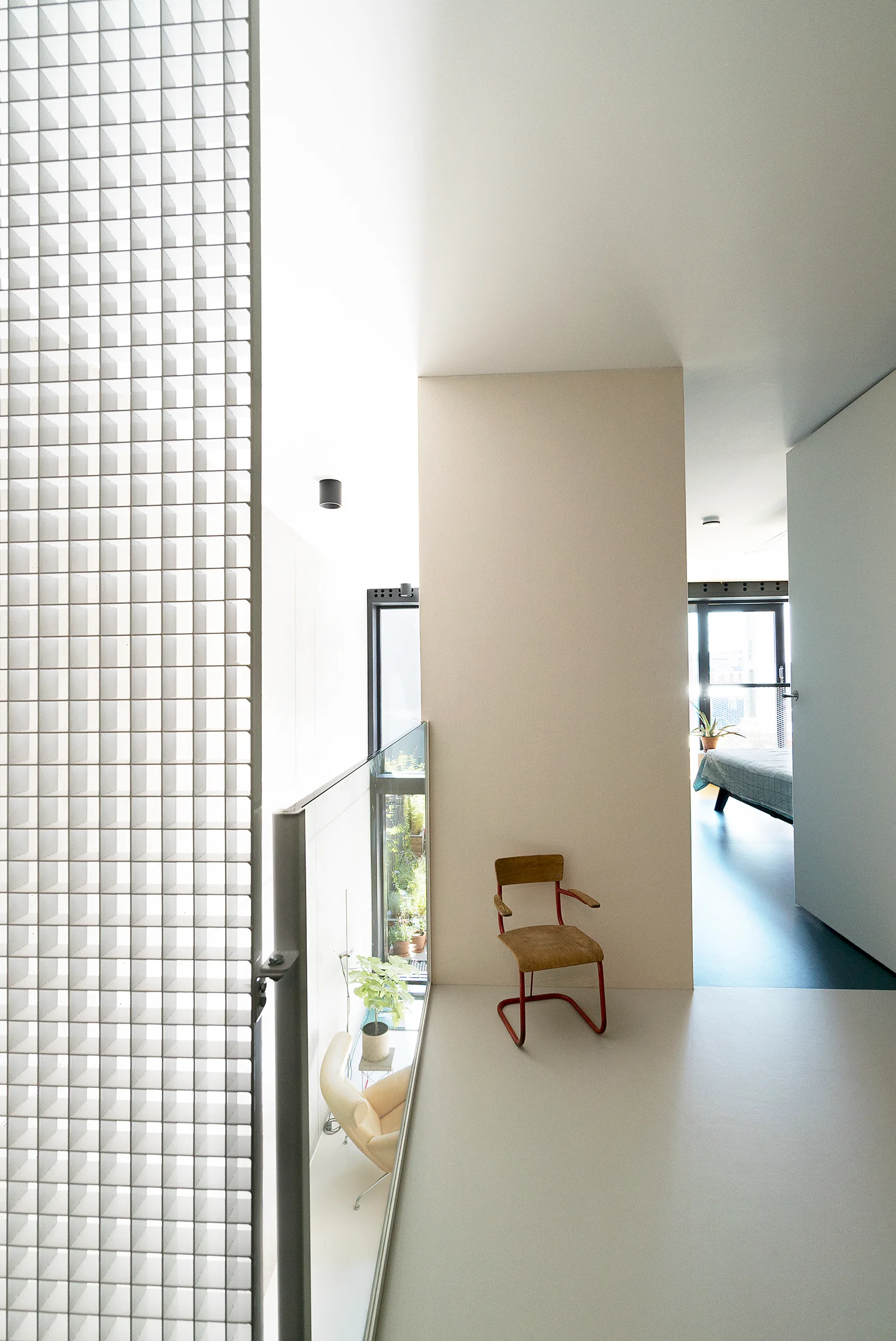 A minimalist landing features a white metal grid screen, a light beige partition wall, a glass railing, and a single wooden chair with a red frame.