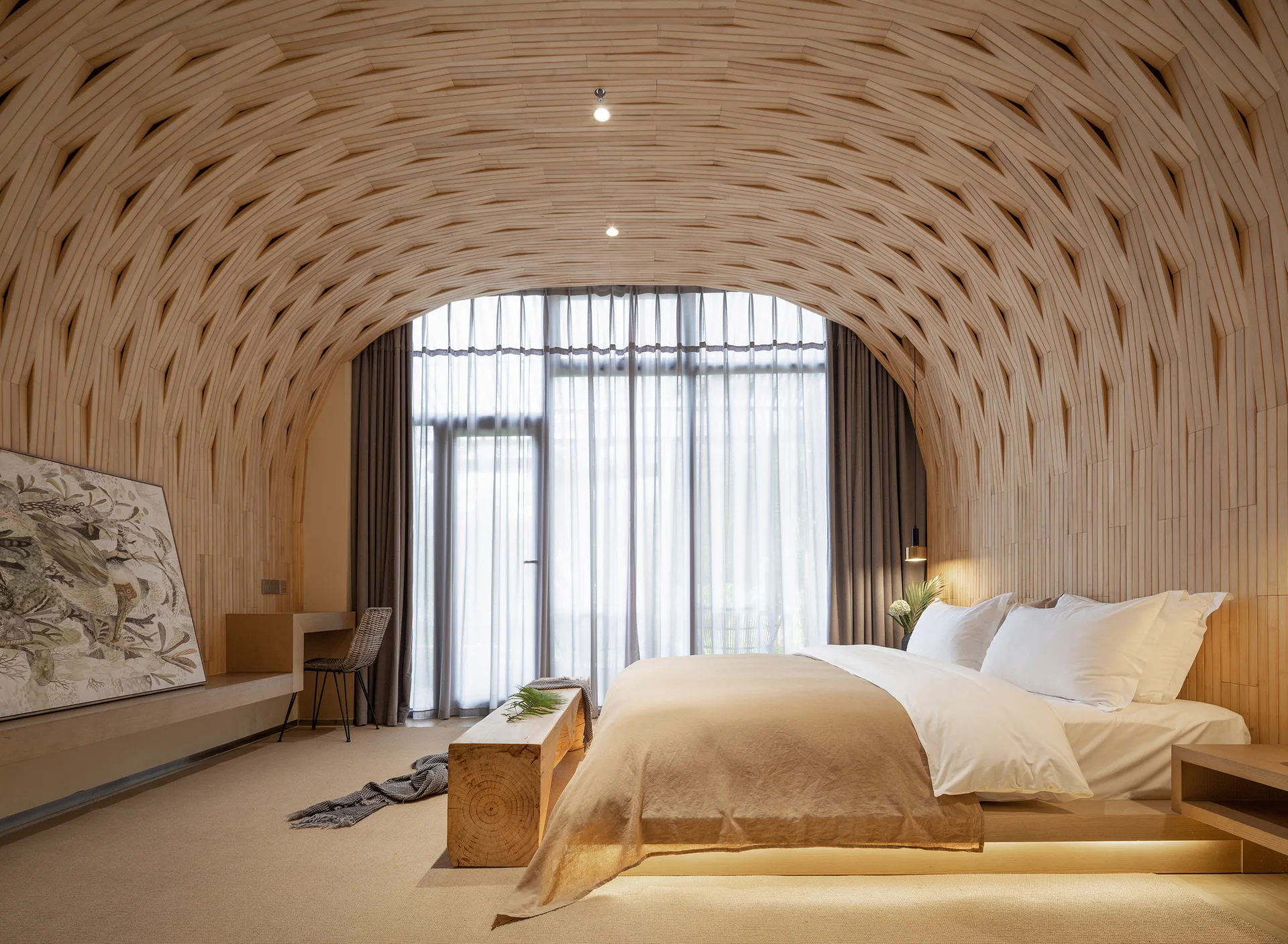 A modern bedroom features a low platform bed beneath a curved wooden lattice ceiling, next to sheer window curtains and a natural wood bench.