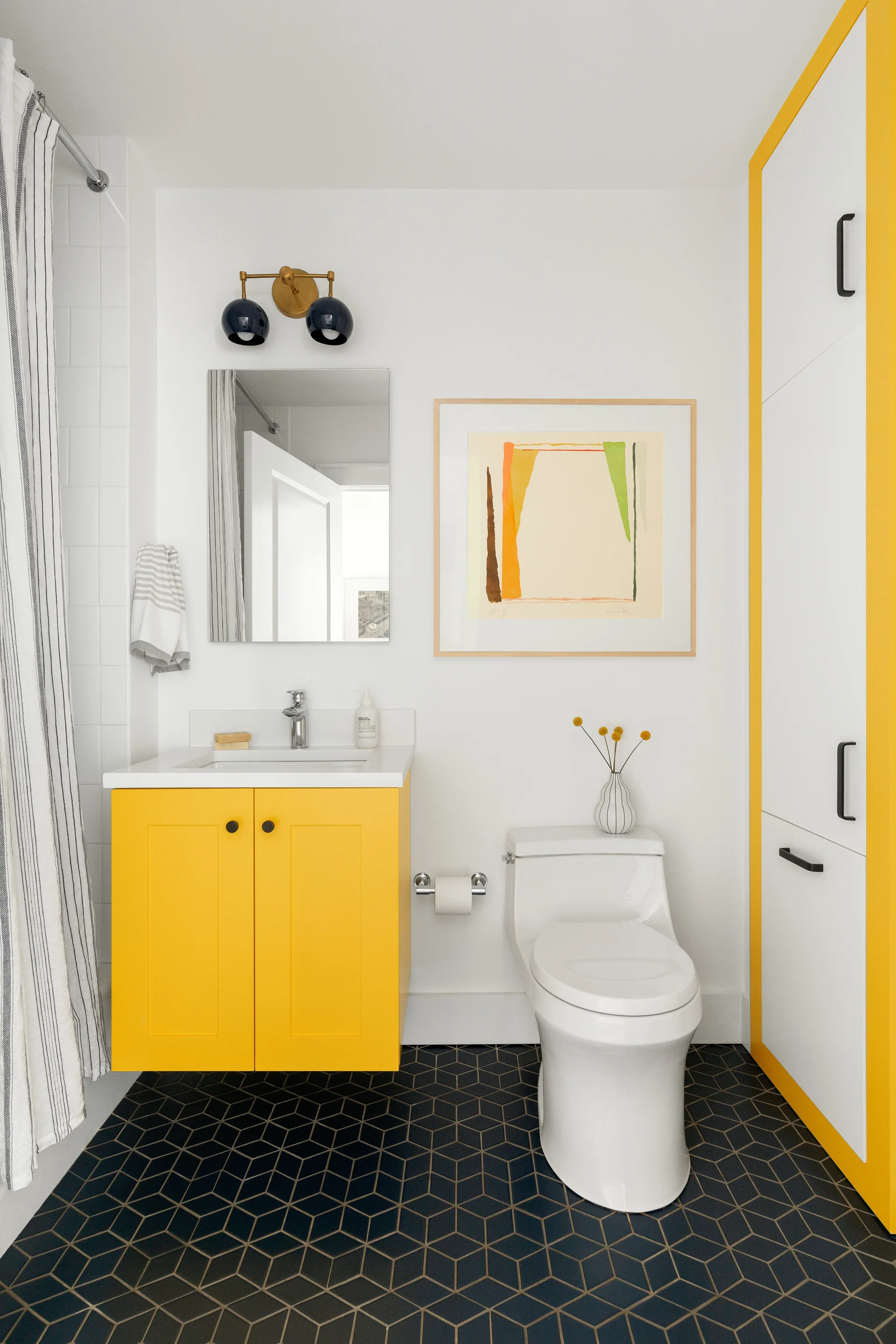 A modern bathroom features a bright yellow floating vanity, a tall cabinet with yellow trim, and black geometric floor tiles.