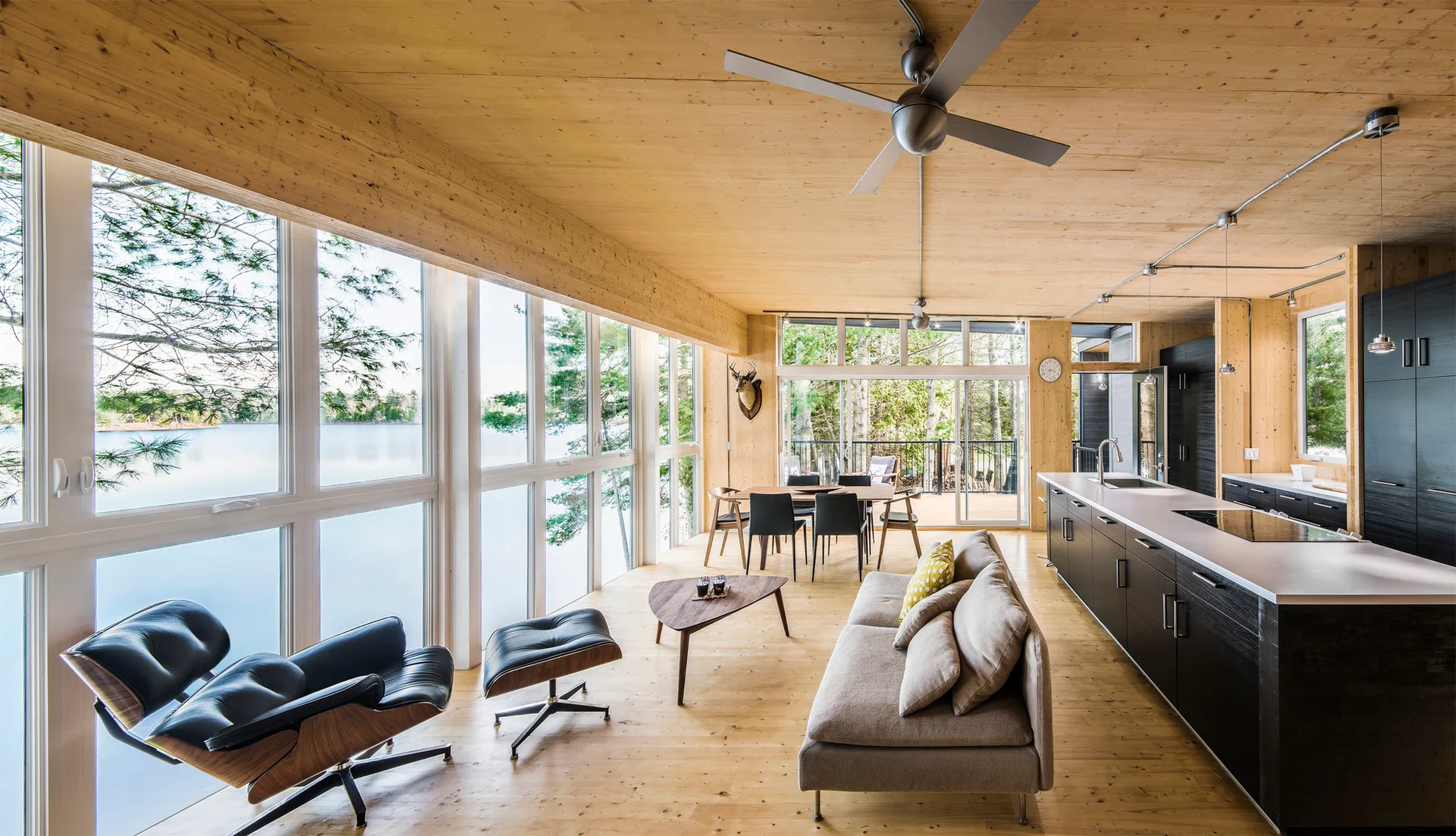 An open living area features light wood paneling on the walls and ceiling, large windows with a lake view, and a dark kitchen island.