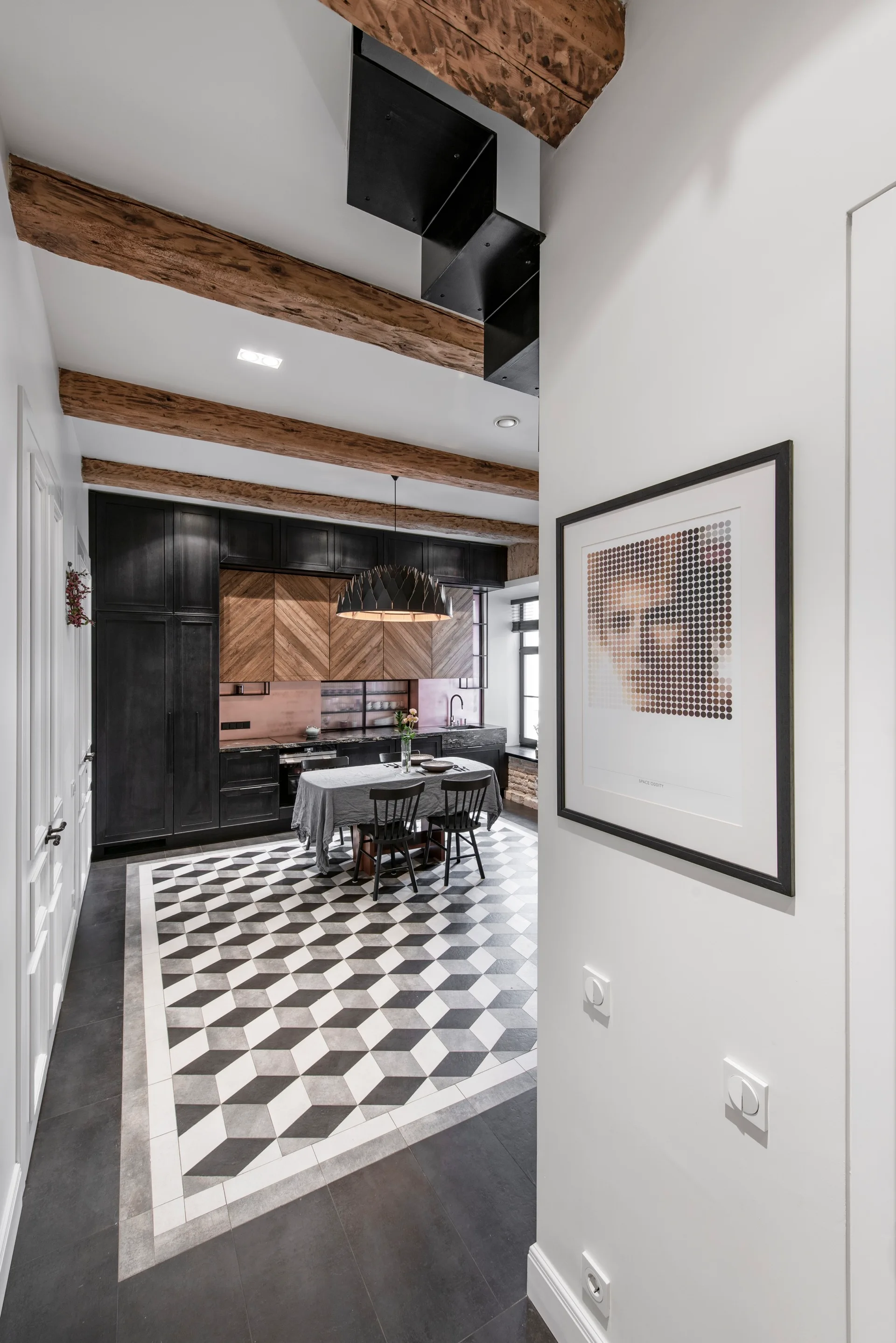 A modern kitchen features black and herringbone wood cabinetry, a geometric cube-patterned tile floor, and rustic ceiling beams.