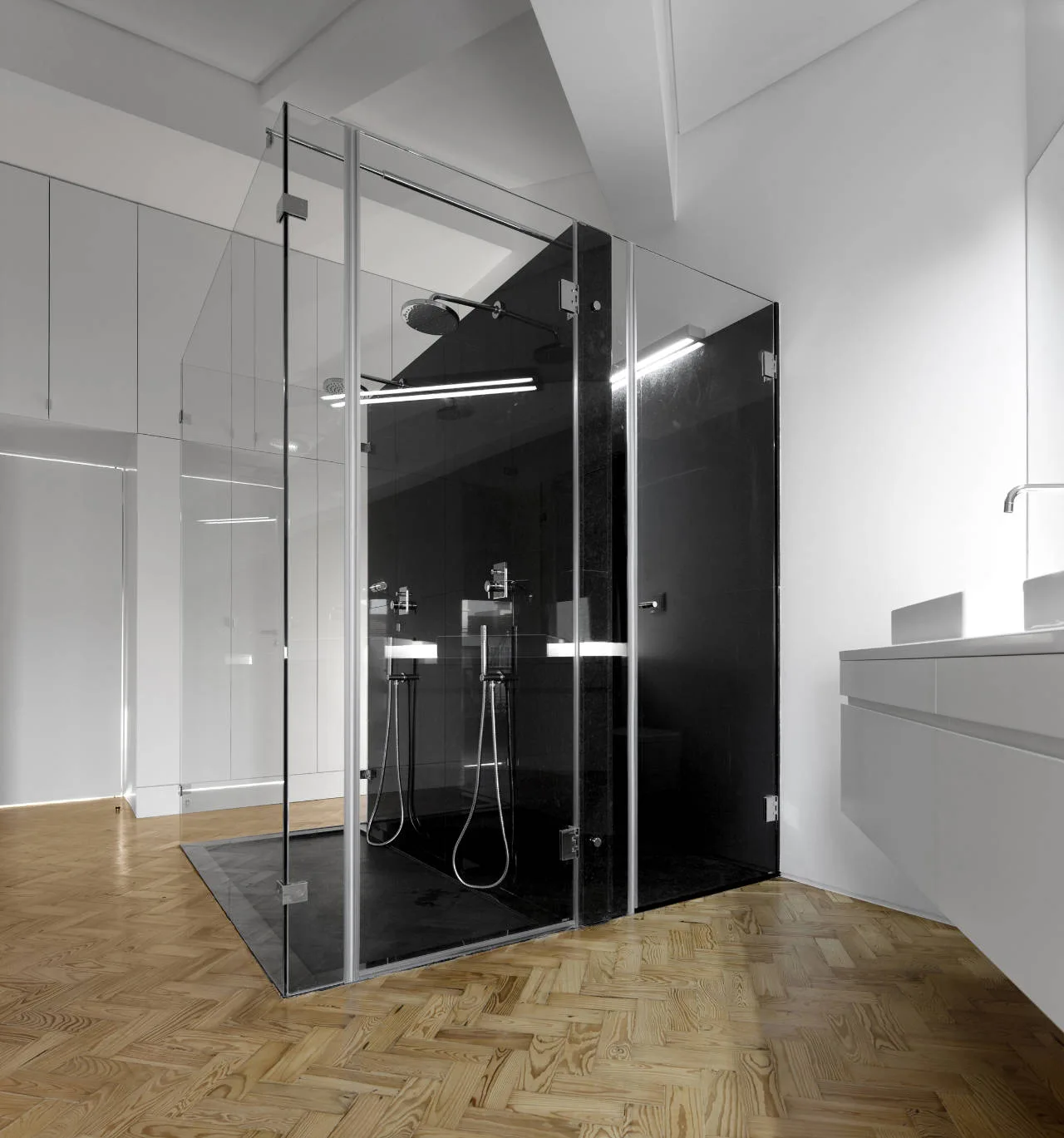 A modern bathroom features a freestanding glass shower enclosure with black tiles on a herringbone pattern wood floor next to a floating white vanity.
