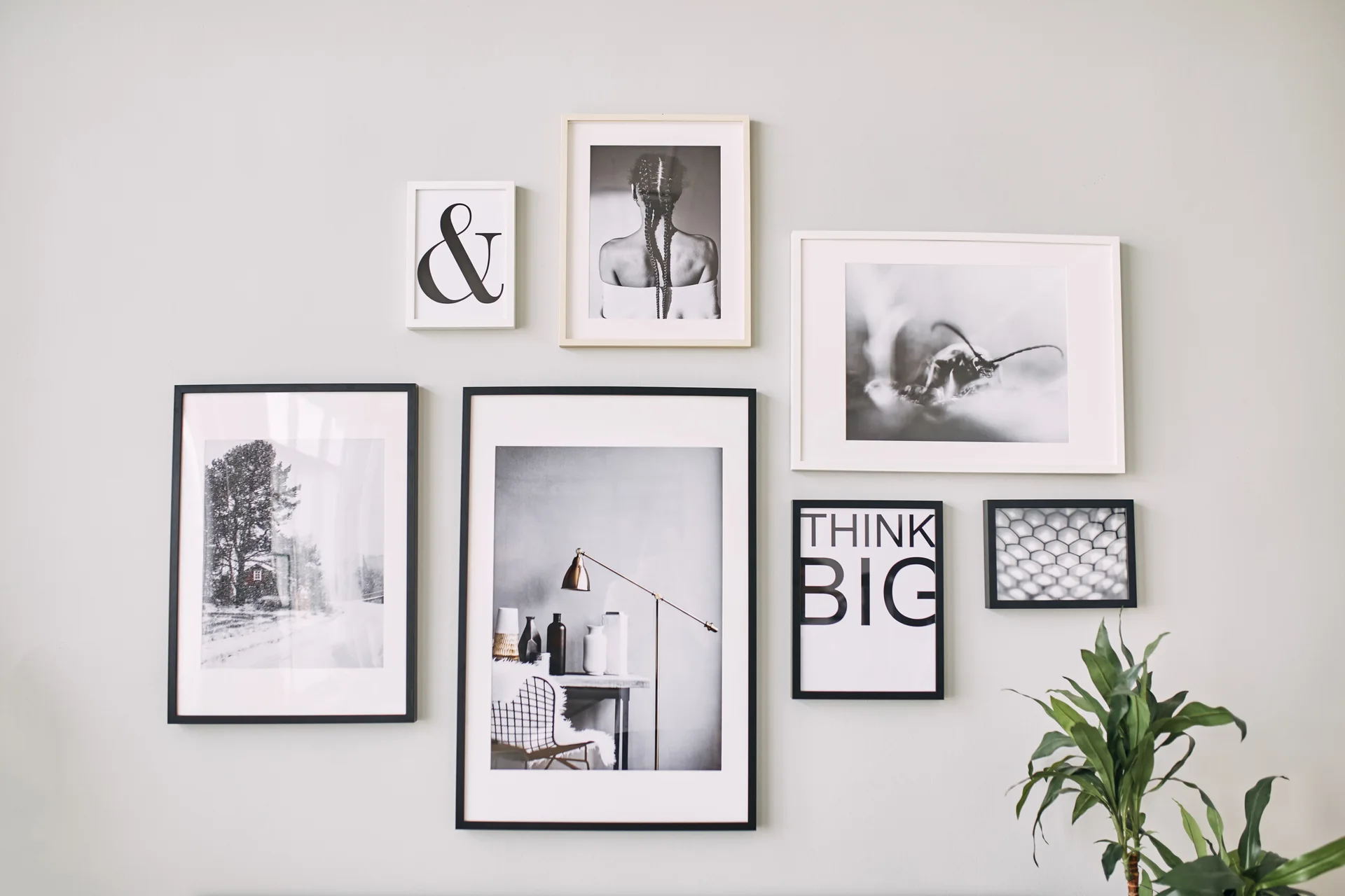 Seven black and white framed art prints in various sizes and frames arranged in an asymmetrical gallery wall layout on a light gray wall.