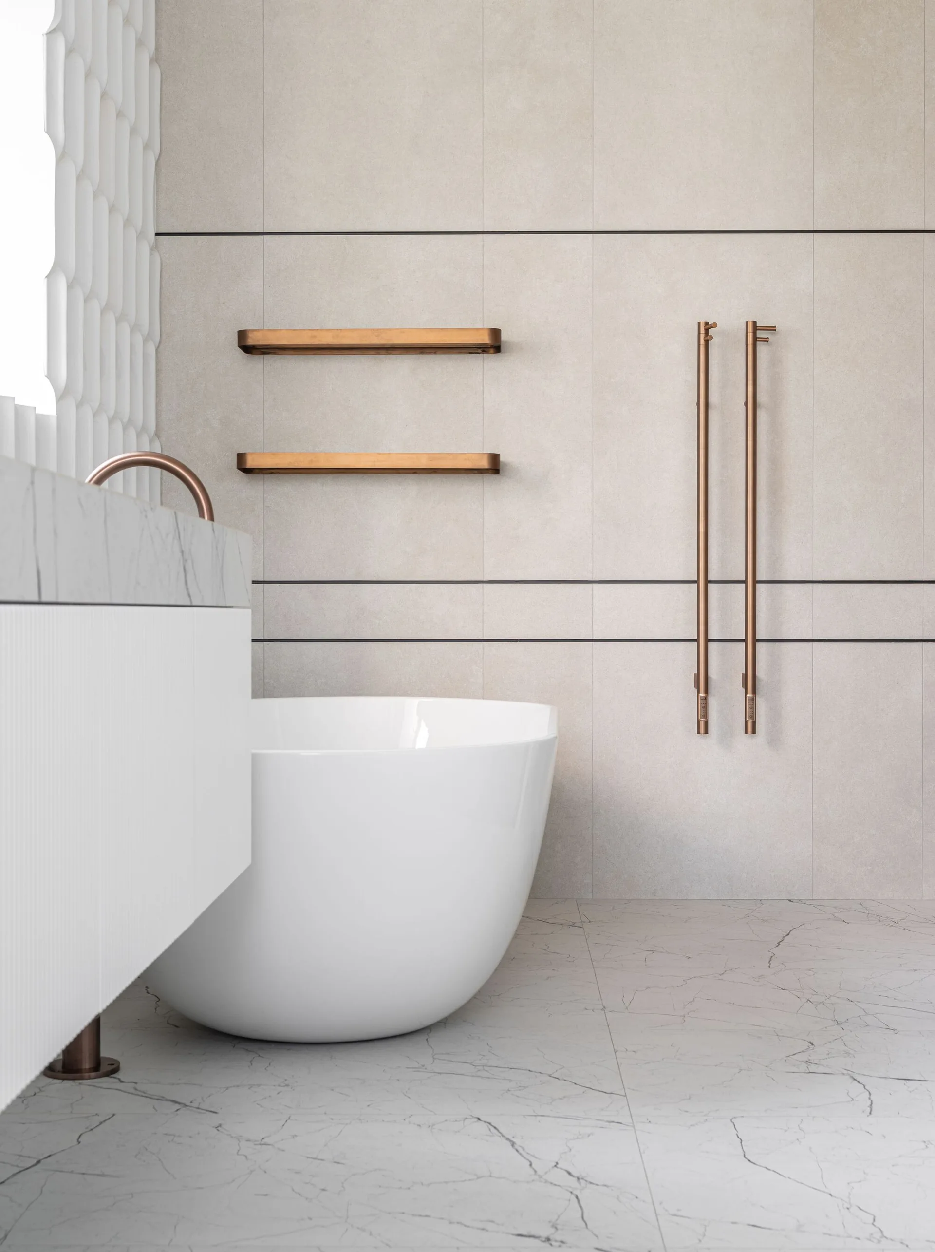A modern bathroom with a white freestanding bathtub, ribbed vanity, large format beige wall tiles, and copper-toned fixtures.
