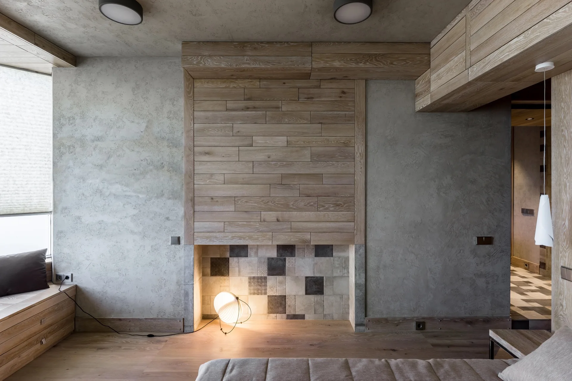 A minimalist bedroom featuring textured grey plaster walls, a wood paneled feature wall with a tiled alcove, and a wooden bench.