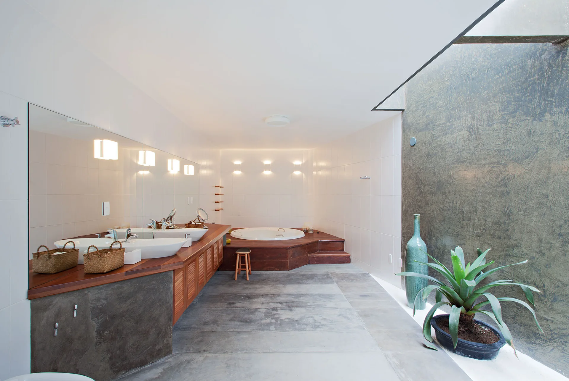 A modern bathroom featuring a long wood vanity with double vessel sinks, a raised round bathtub, and grey concrete flooring.