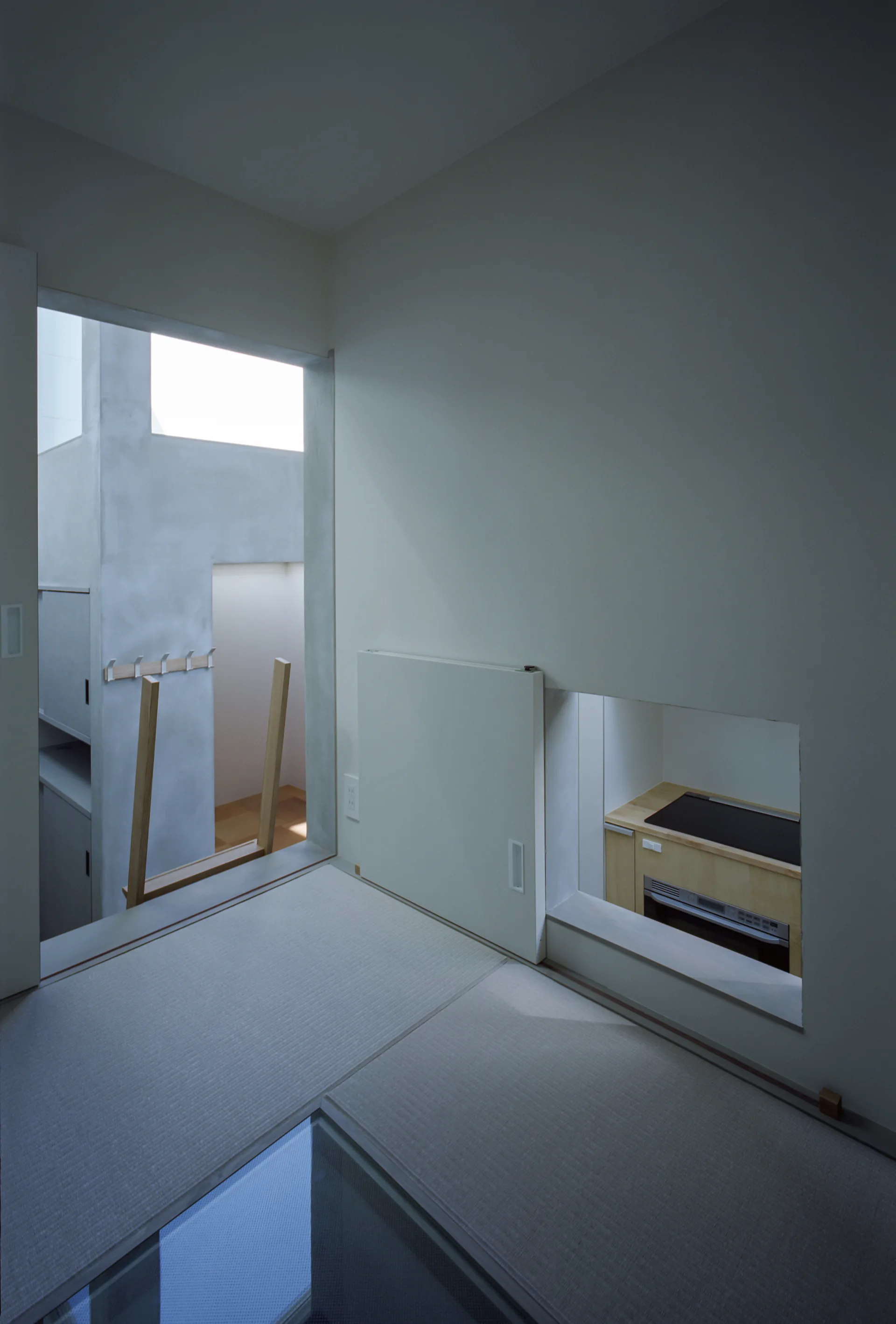 A minimalist room featuring woven tatami floor mats, an open doorway, and a white sliding door that covers a wall cutout looking into a small kitchen.