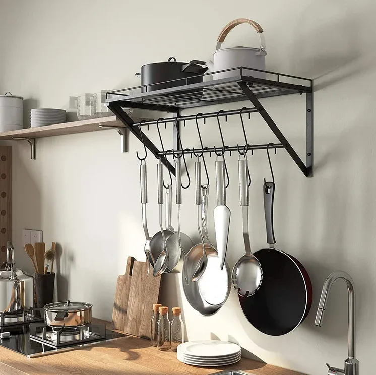 A black metal wall-mounted pot rack with hanging pans and cooking utensils is positioned above a wooden kitchen countertop.