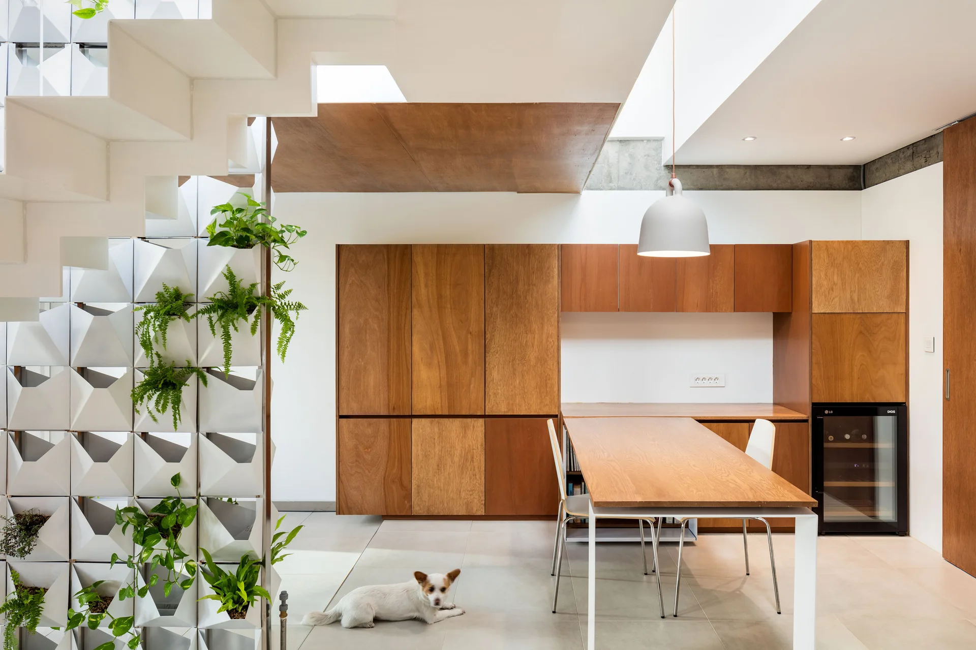 A modern kitchen featuring warm wood cabinetry, a matching dining table, and a white sculptural staircase with integrated vertical planters.