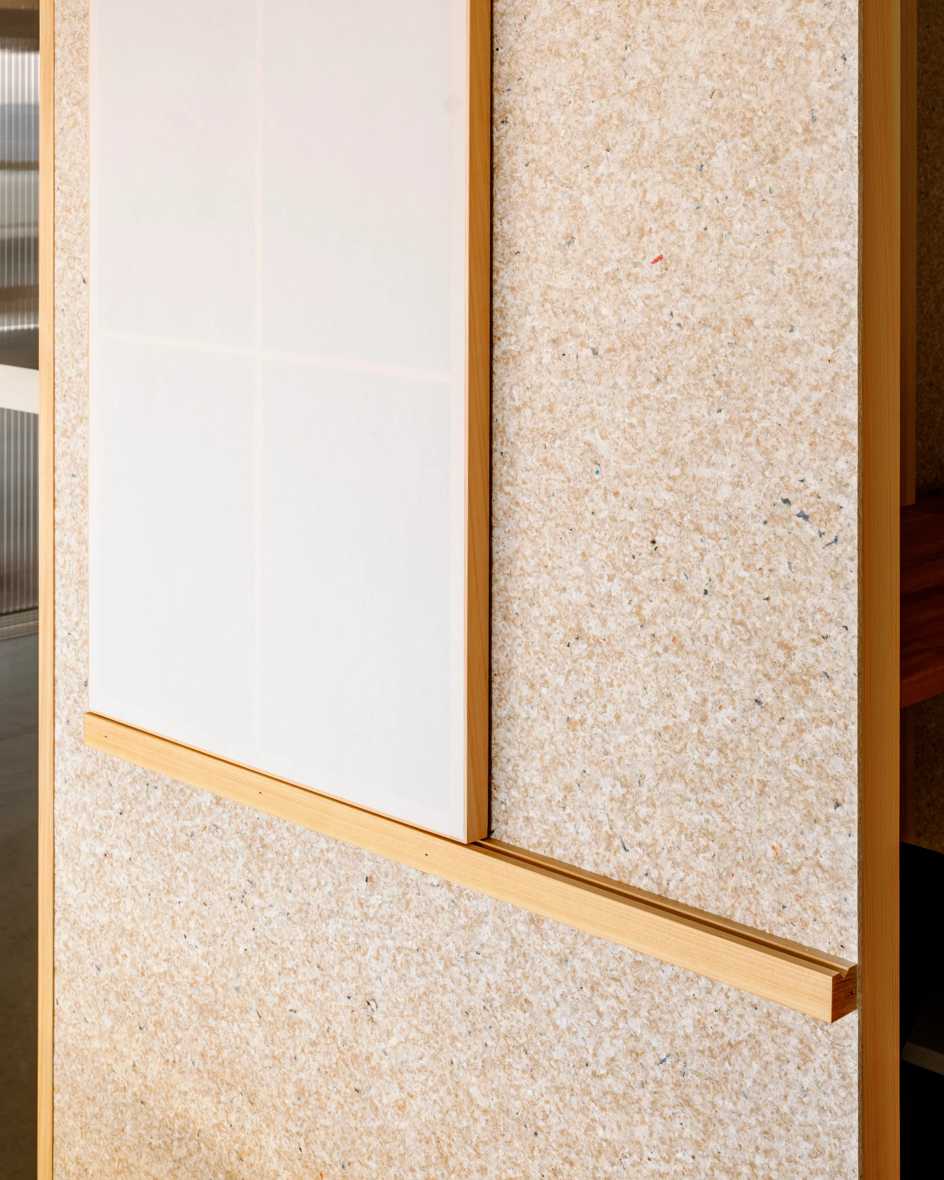 A close-up of a speckled beige composite wall panel featuring a horizontal light wood track and a sliding white screen panel.