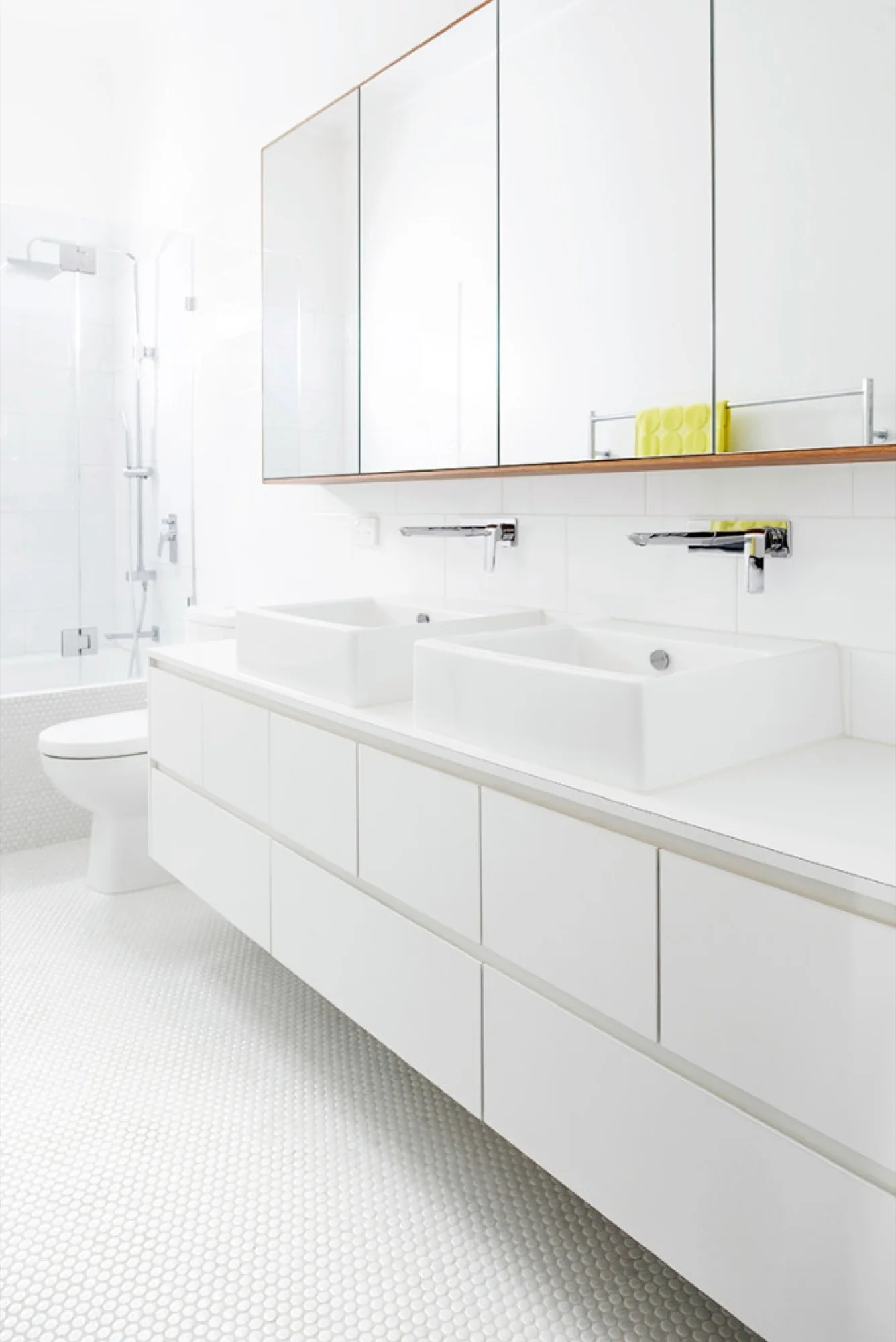 A bright white bathroom featuring a floating double vanity with vessel sinks, wall-mounted faucets, a large mirrored cabinet, and penny tile flooring.