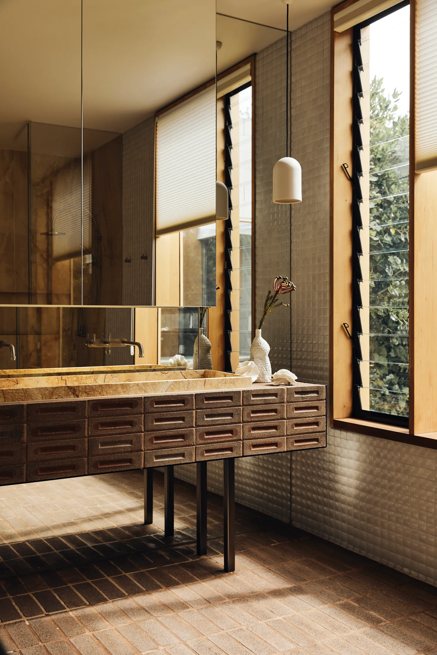 A modern bathroom features a brick-clad floating vanity with a stone sink, vertical louvered windows in wood frames, and small square wall tiles.