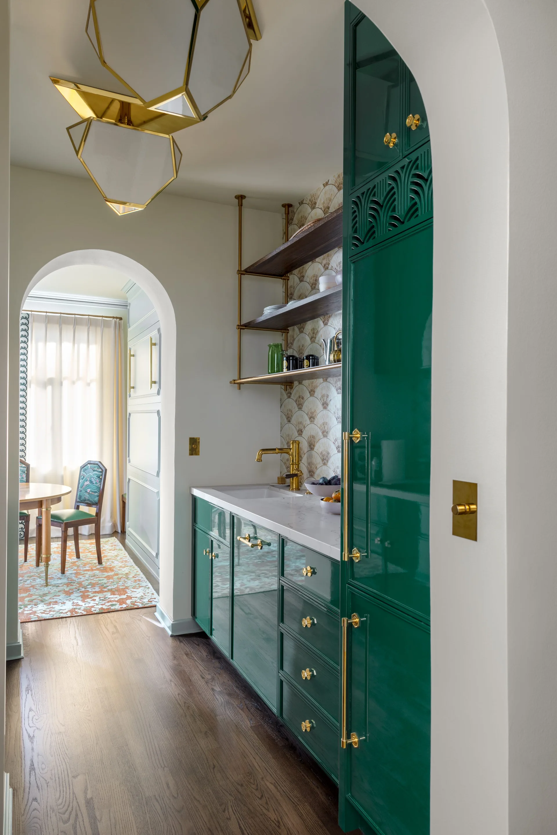A kitchen pantry featuring high-gloss emerald green cabinets, a white countertop, brass hardware, and a scalloped wallpaper backsplash.