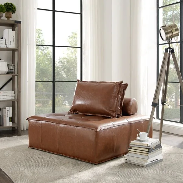 A low-profile cognac leather modular chair sits on a geometric rug in front of large black-framed windows with sheer curtains.