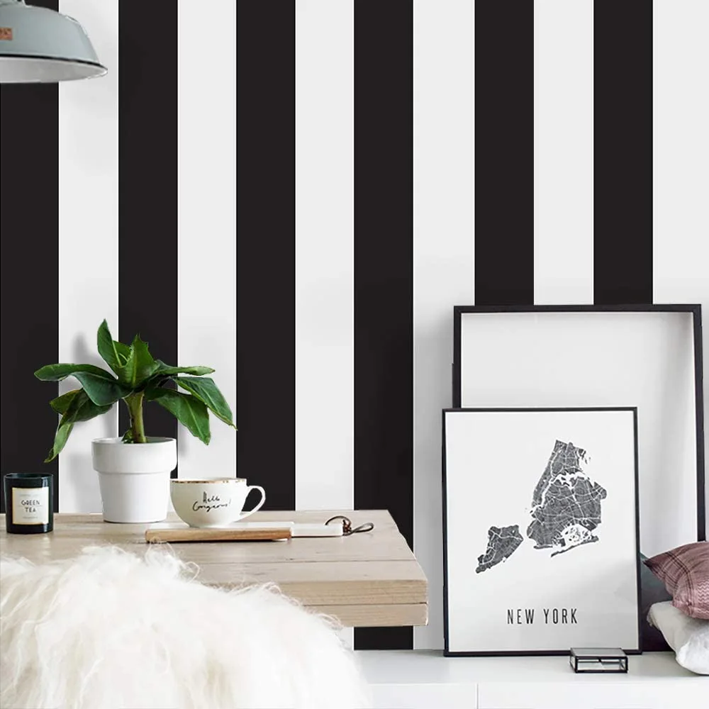 A wooden desk sits against a black and white striped wall with a framed map of New York and a small potted plant.
