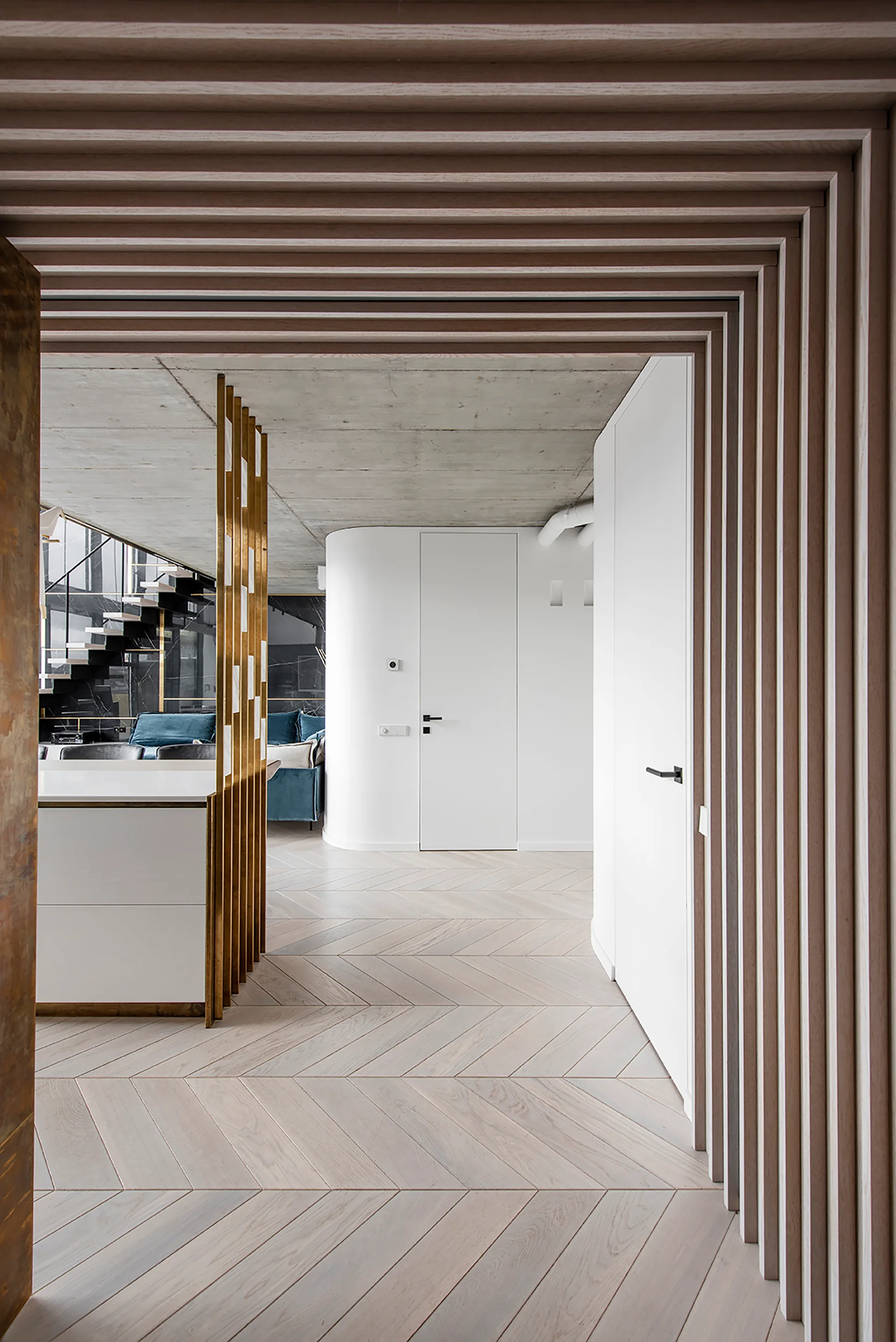A minimalist hallway features light wood herringbone flooring, white curved walls, and distinctive wood slat detailing on the ceiling and wall.