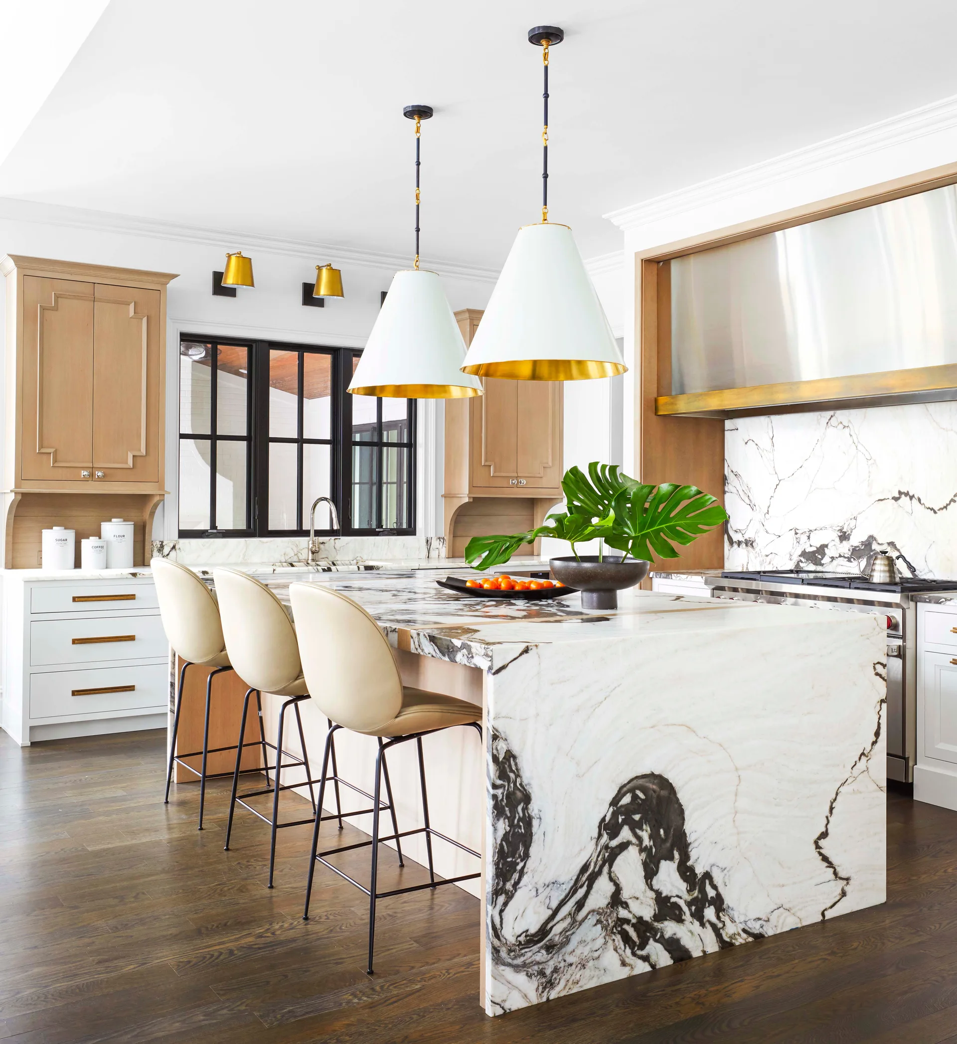 A spacious kitchen features a large waterfall marble island with dramatic veining, white pendant lights, three barstools, and wood-toned cabinetry.
