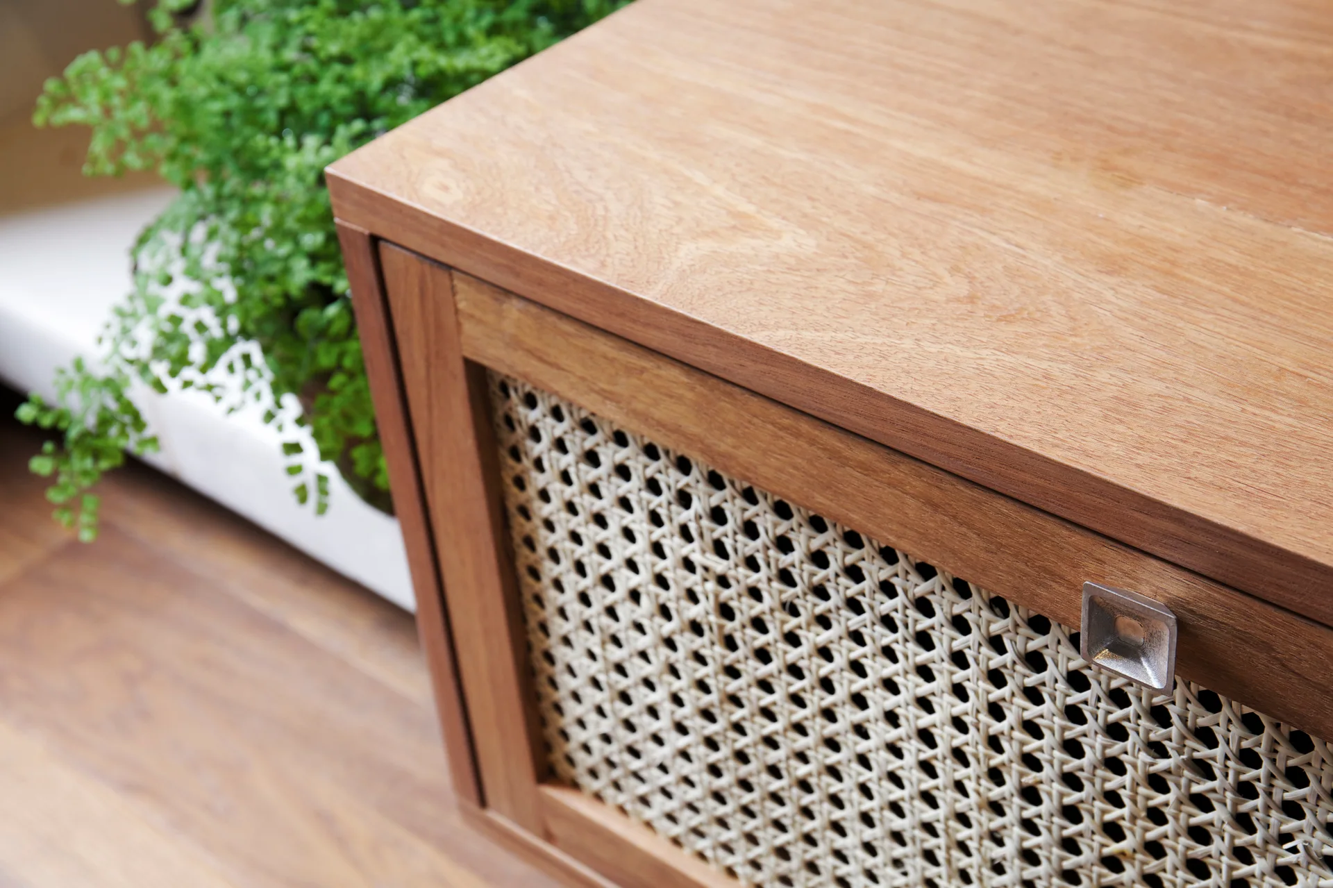 A close-up of a warm wood cabinet featuring a door with light-colored woven cane webbing and a small silver square pull handle.