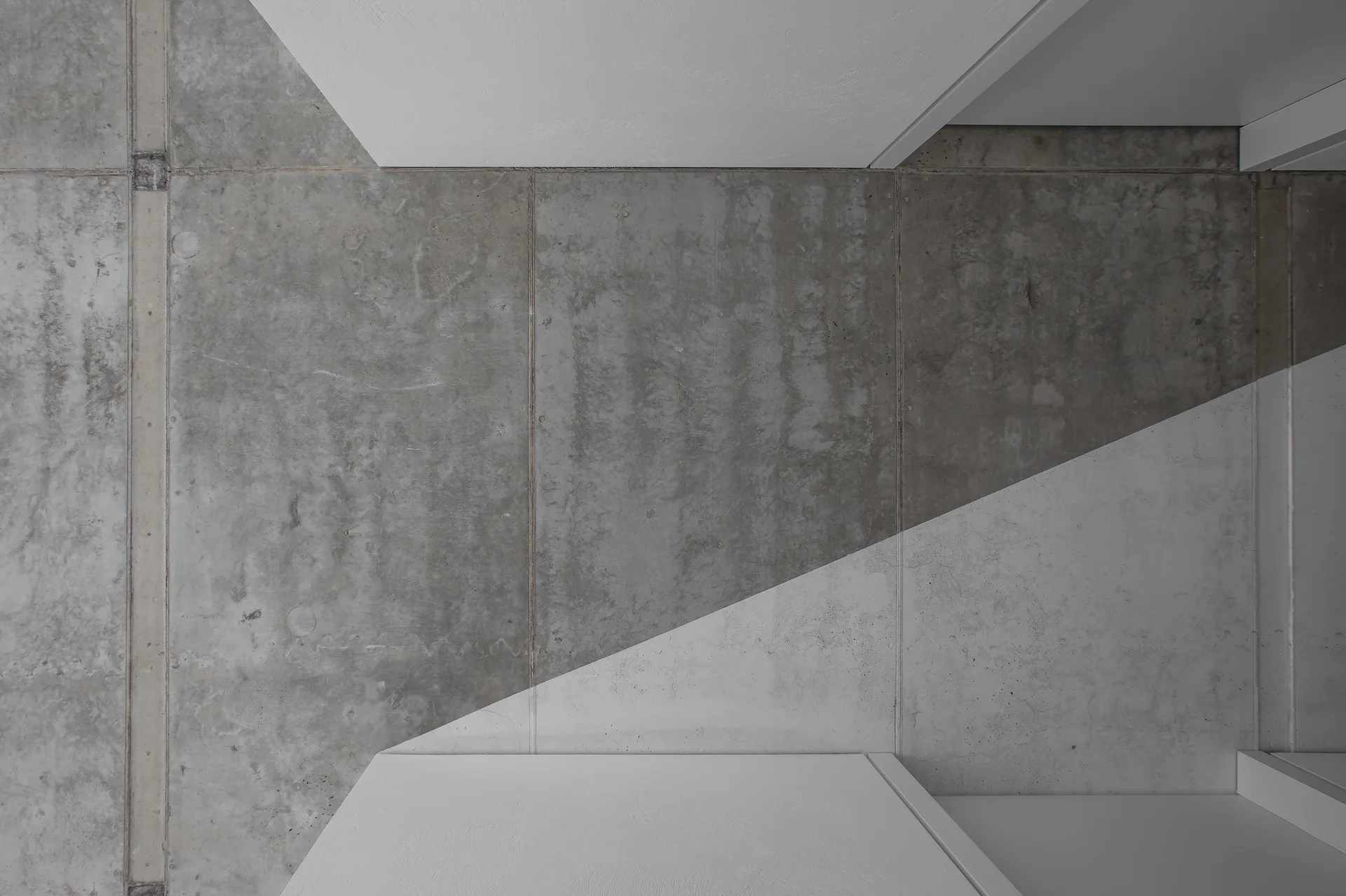 A top-down view of textured grey concrete wall panels meeting smooth white geometric architectural structures.