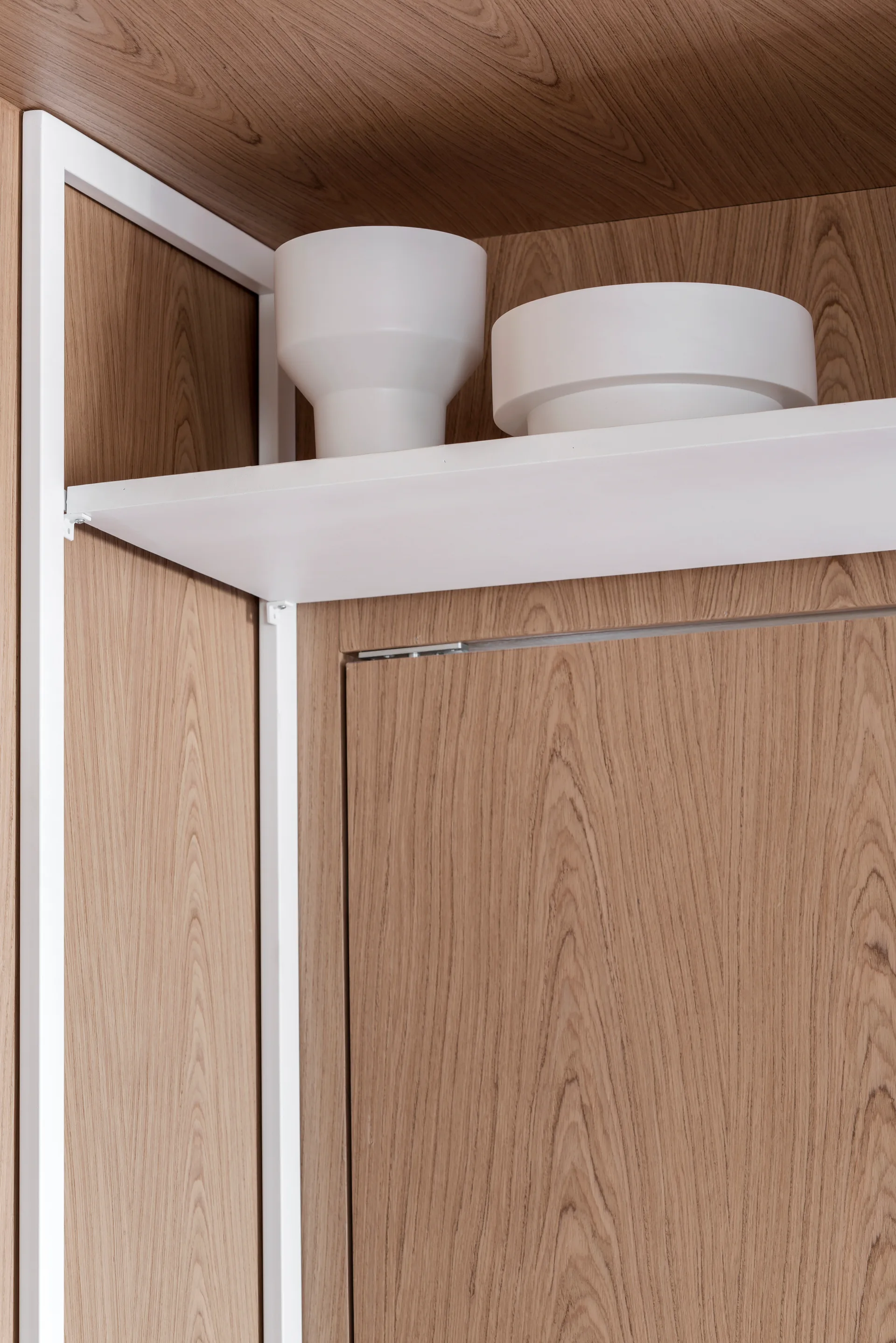 A close-up of a minimalist wood paneled wall featuring a white metal structural frame, shelf, and two white ceramic decorative bowls.