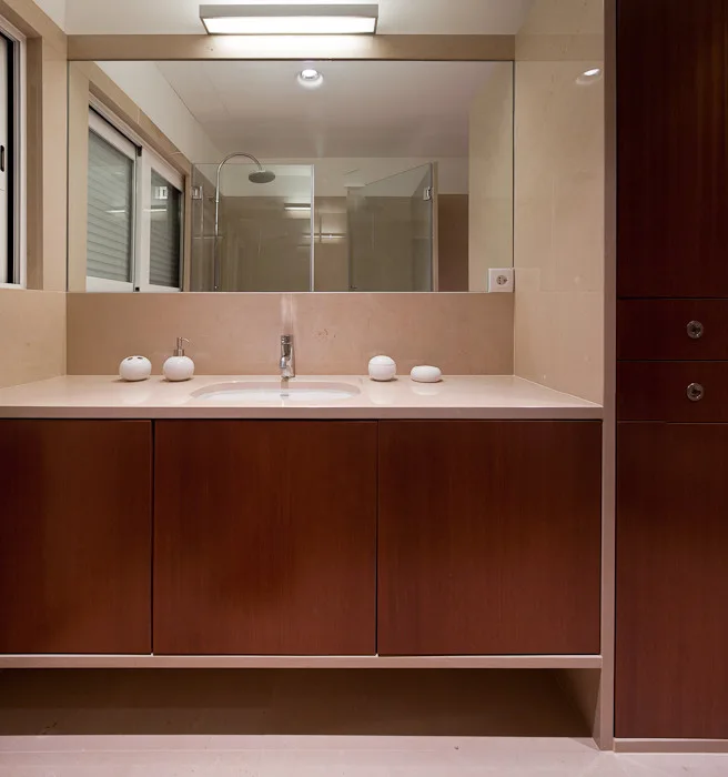 A minimalist bathroom features a floating dark wood vanity under a large mirror, set against beige stone walls.