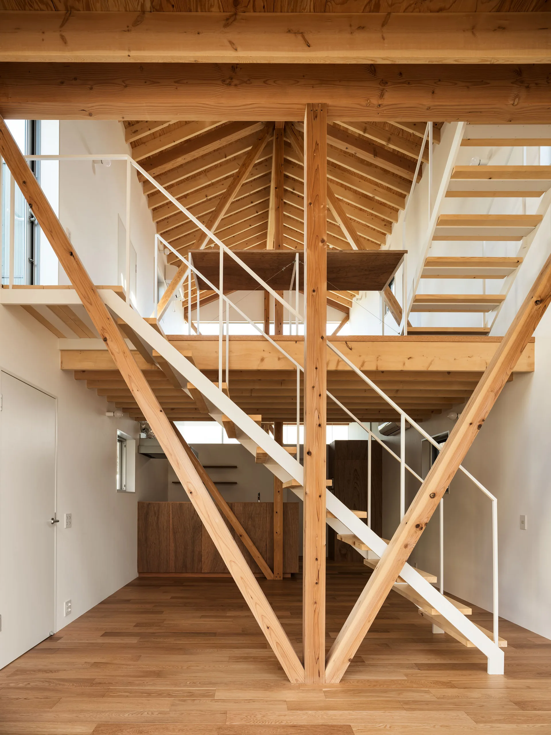 A symmetrical timber-frame interior features a central wooden staircase with white metal railings beneath an exposed wood rafter ceiling.