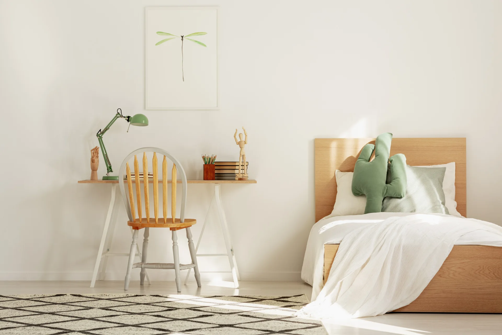 A bright kids bedroom features a light wood platform bed with white bedding, a matching trestle desk with a green desk lamp, and a geometric area rug.