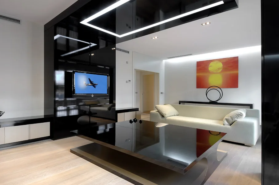 A modern living room features a glossy black wall paneling system, a low black coffee table, a light-colored sofa, and a colorful sunset painting.