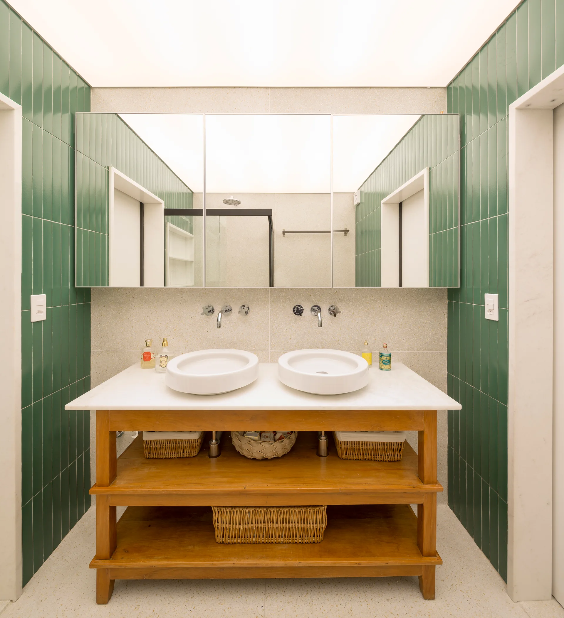 A modern bathroom features a wooden double vanity with white vessel sinks, set against vibrant green vertical wall tiles and a large mirrored cabinet.