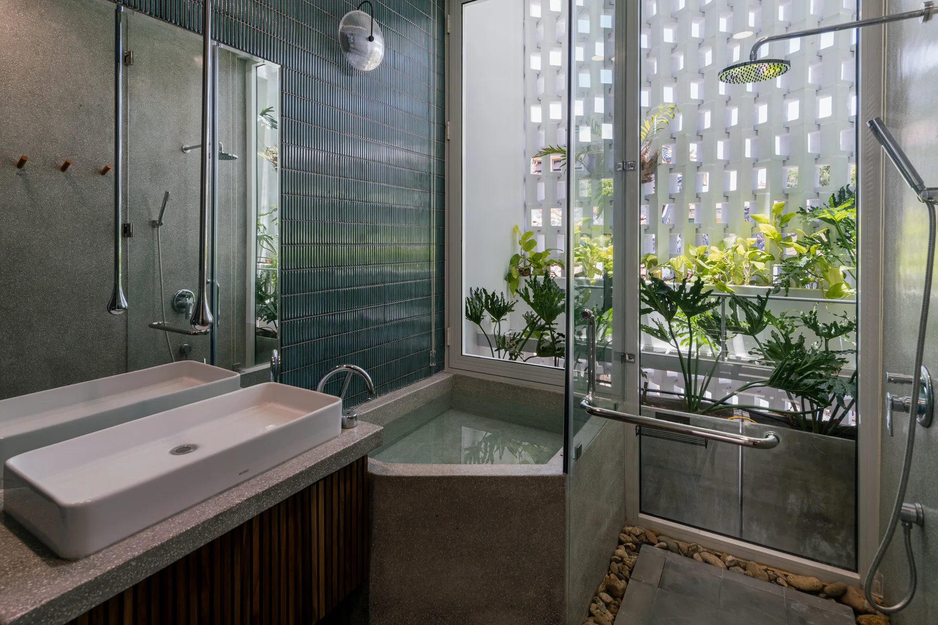 A modern bathroom featuring a white vessel sink on a concrete vanity, a built-in tub, and a glass wall looking out at plants and a breeze block screen.