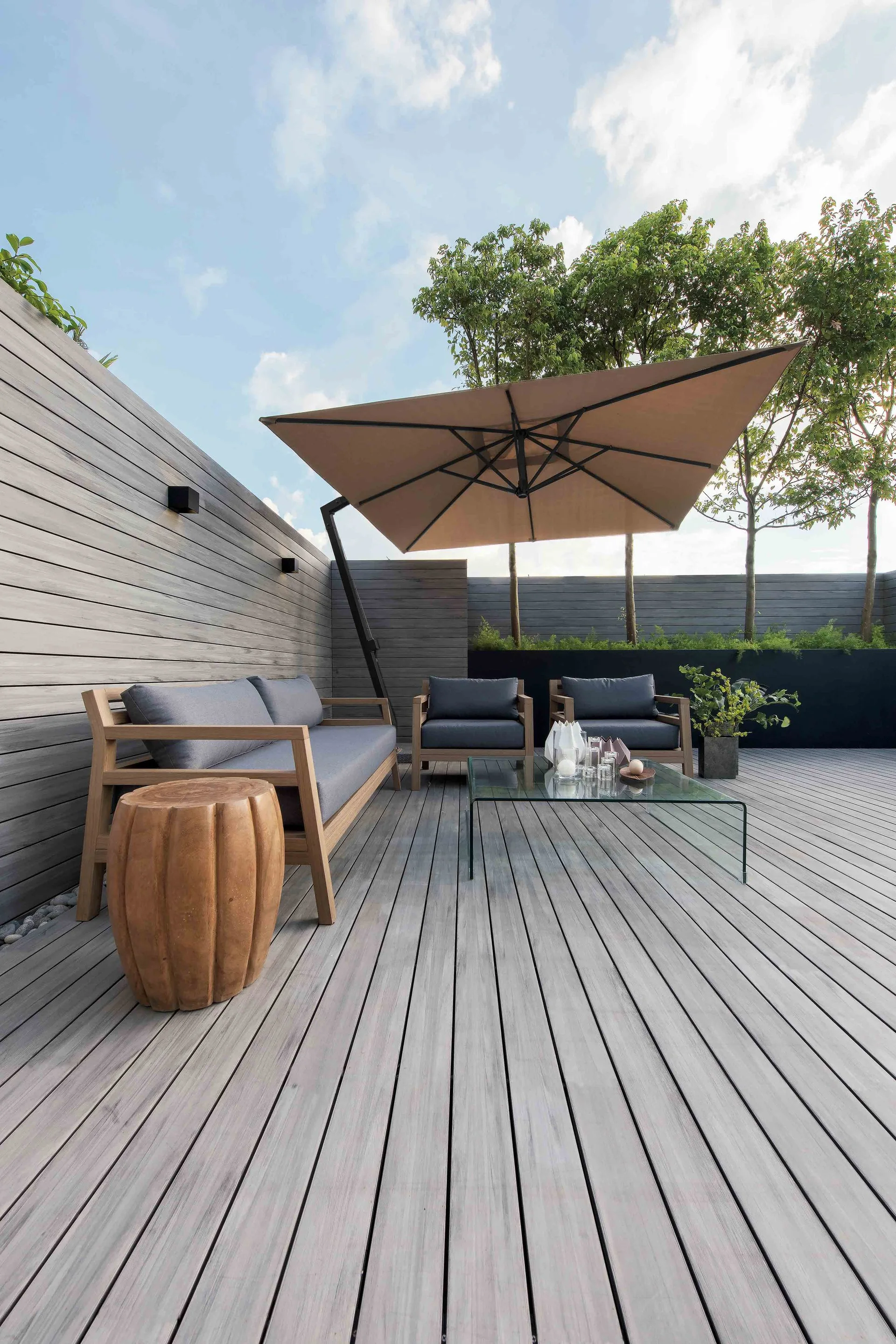 An outdoor terrace features grey wood decking, modern wood lounge furniture with grey cushions, and a large tan cantilever umbrella.