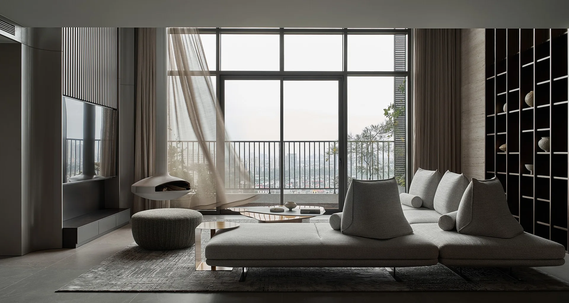 A modern minimalist living room features a low grey sectional sofa, a hanging fireplace, and floor-to-ceiling windows leading to a balcony.